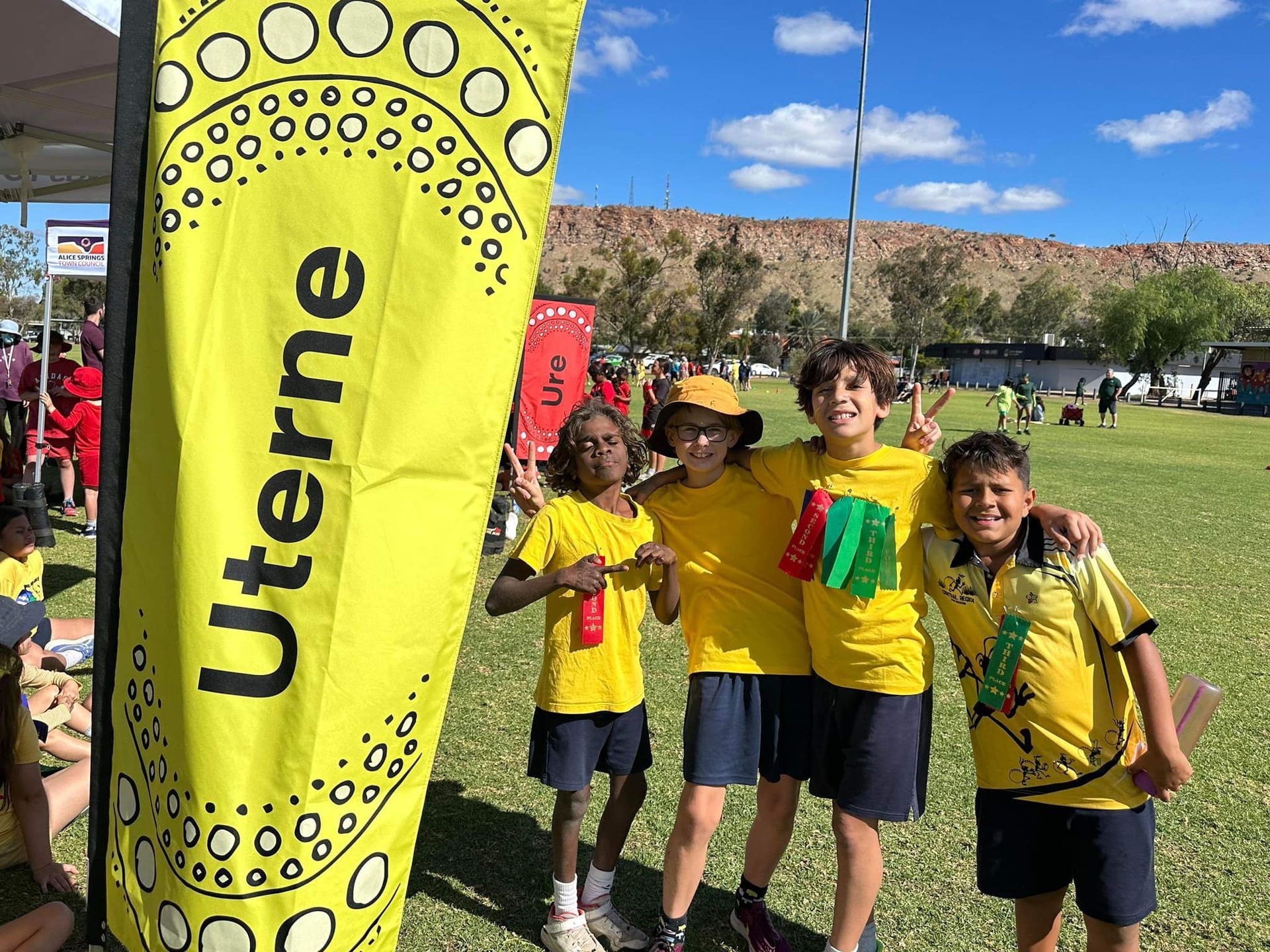 Four smiling children in yellow shirts pose by a 