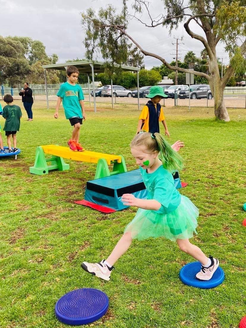 Children in green shirts and tutus playing on balance equipment in a park.