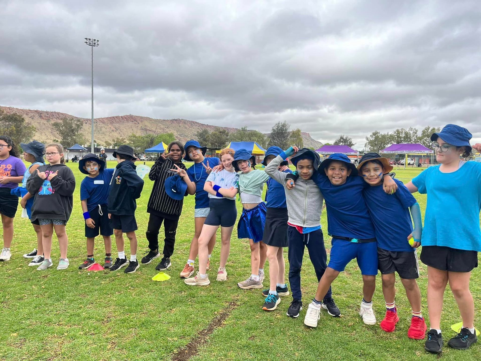 Children in blue uniforms on a grassy field; some smiling, posing, and hugging.