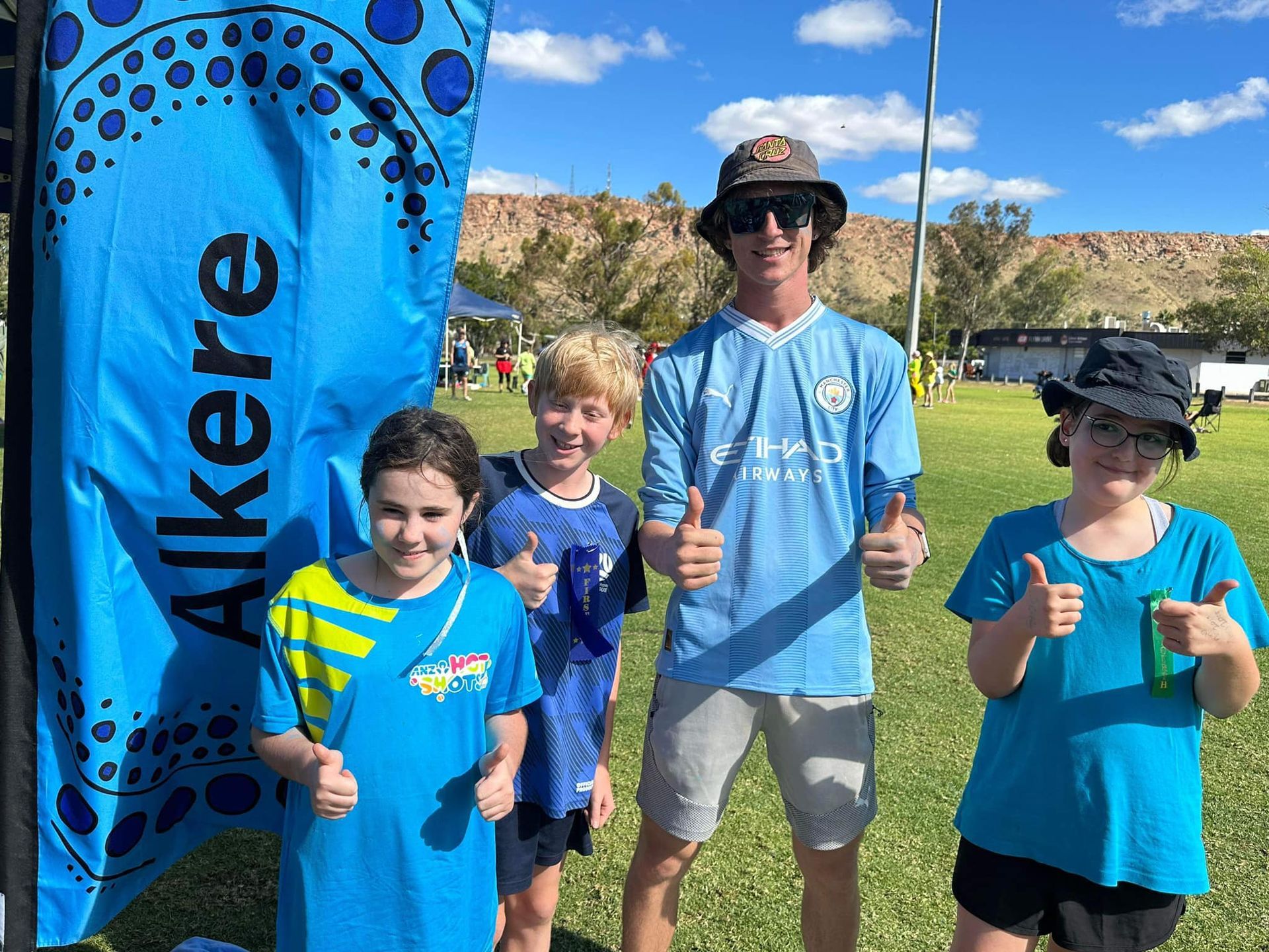 Four people smiling with thumbs up. Blue flag with 