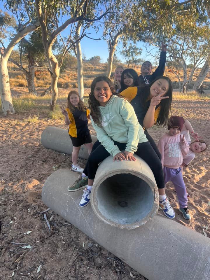 Group of children playing on concrete tubes in a park, posing and smiling.