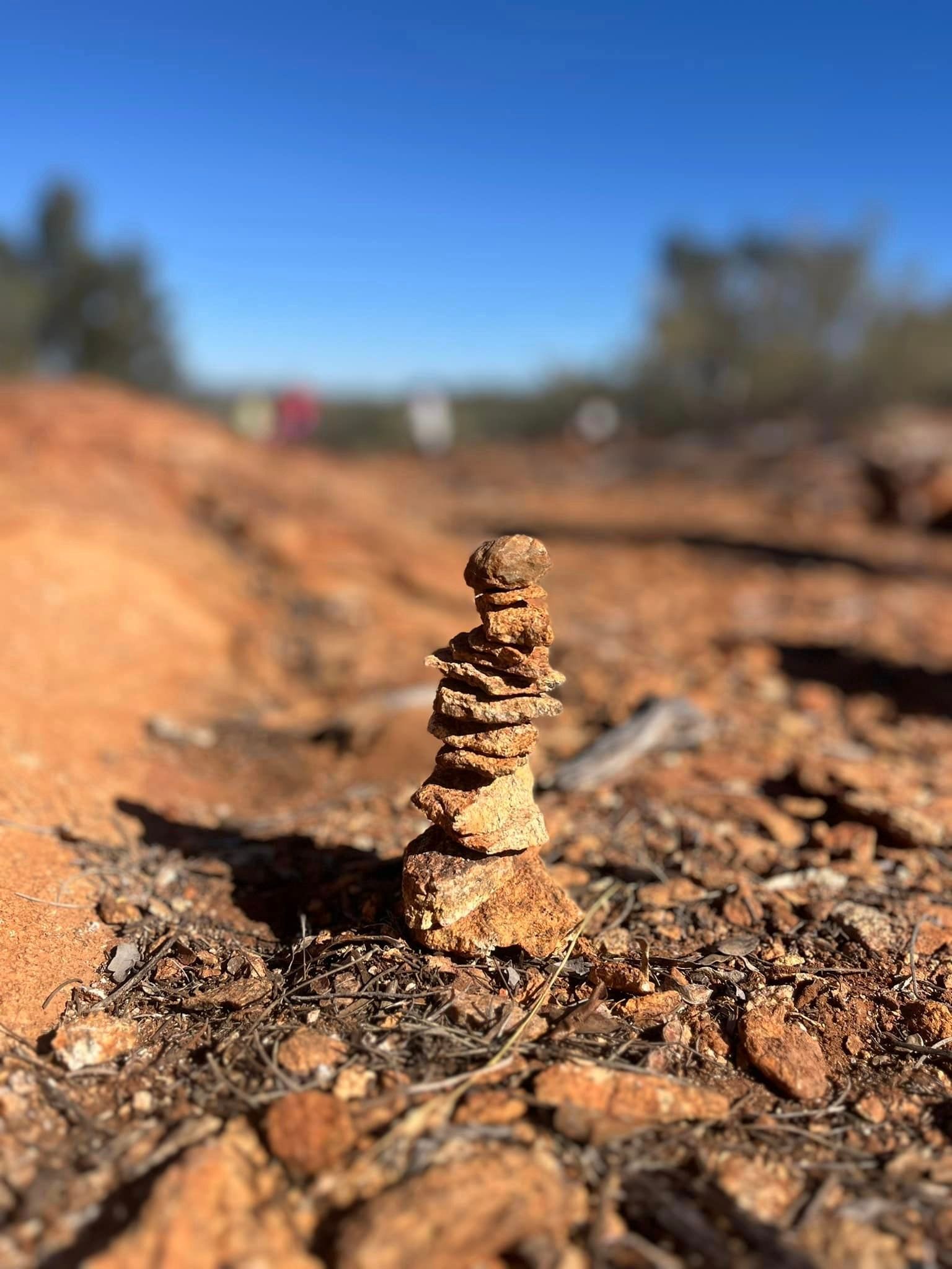 Stack of small, brown stones on reddish dirt path under a clear blue sky.