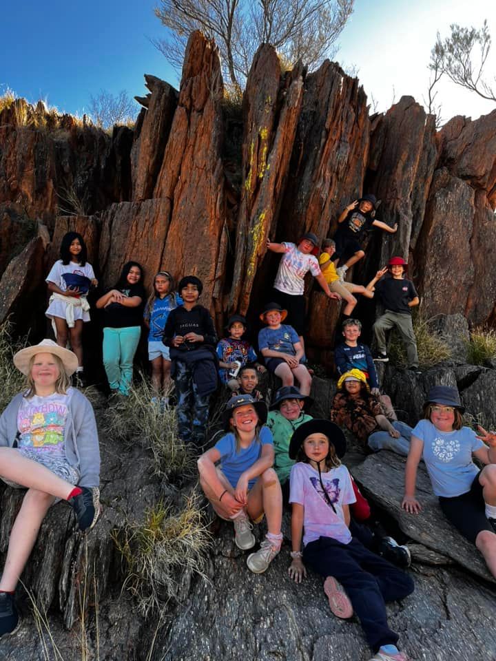 Group of children posing on red rock formation, blue sky.