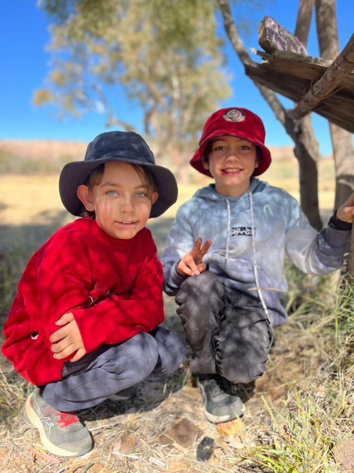 Two children crouching outdoors, wearing hats and colorful clothing, smiling.