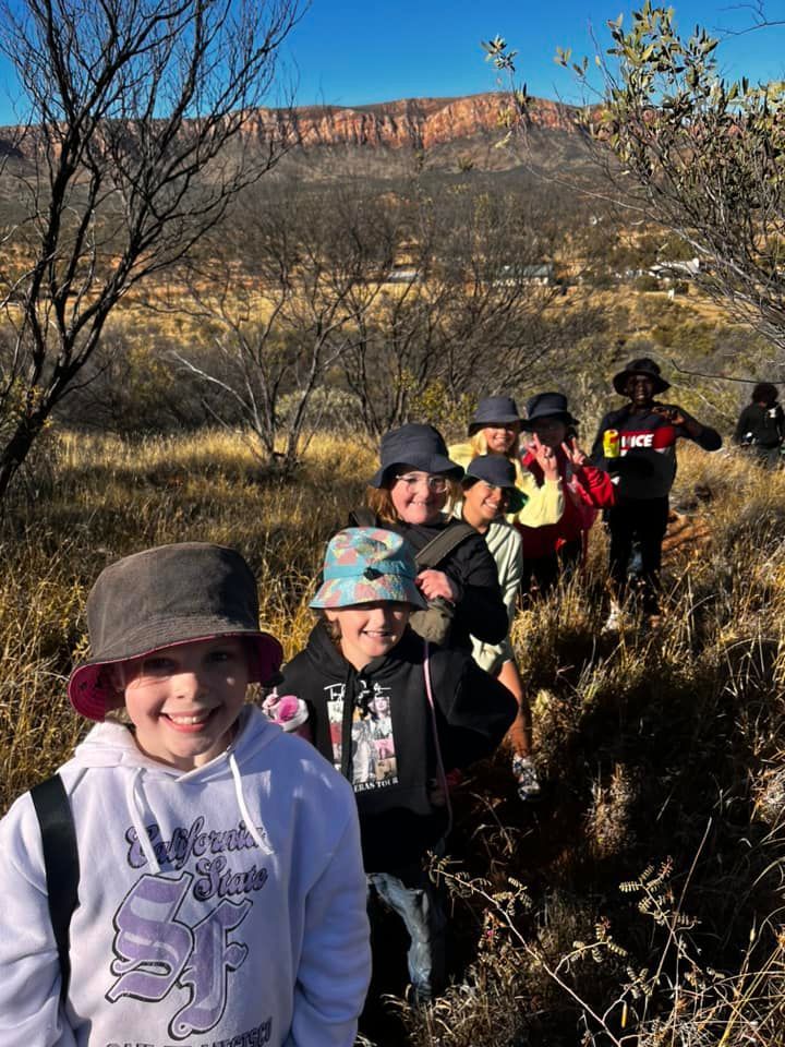 Group of kids hiking in a sunny, arid landscape with a mountain in the background.