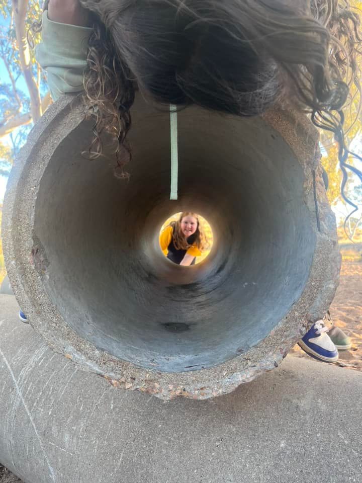 Person looking through a concrete tube at another person smiling; outdoors.
