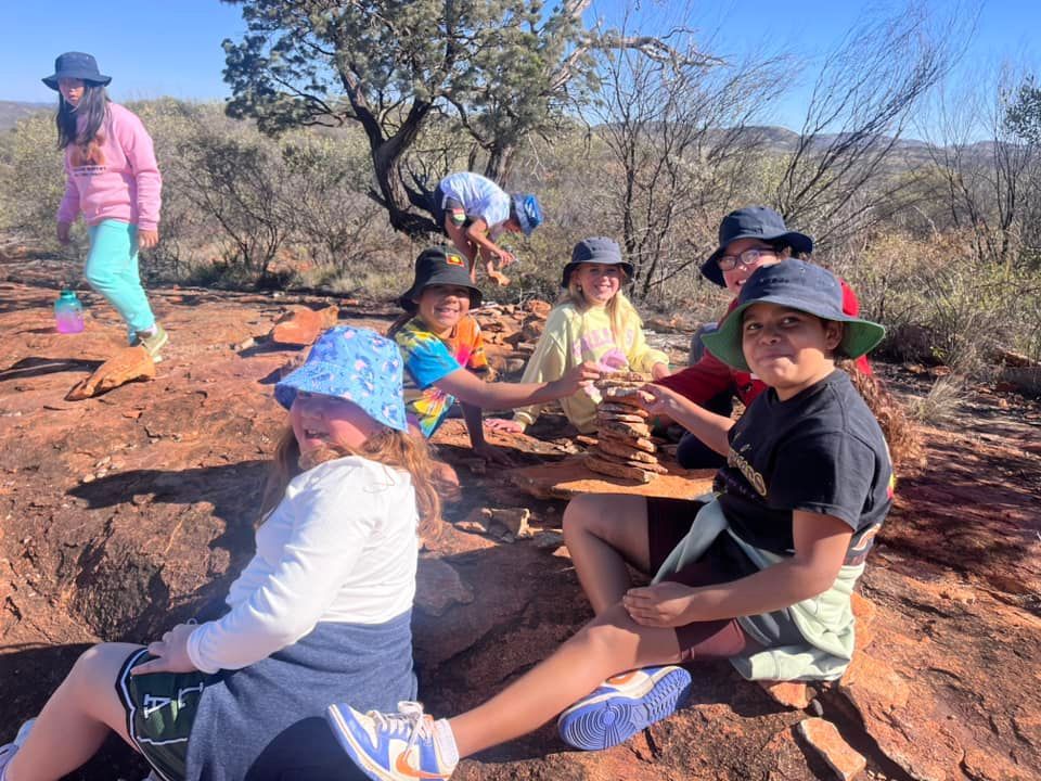 Group of kids building a rock tower outdoors in a sunny, natural setting.