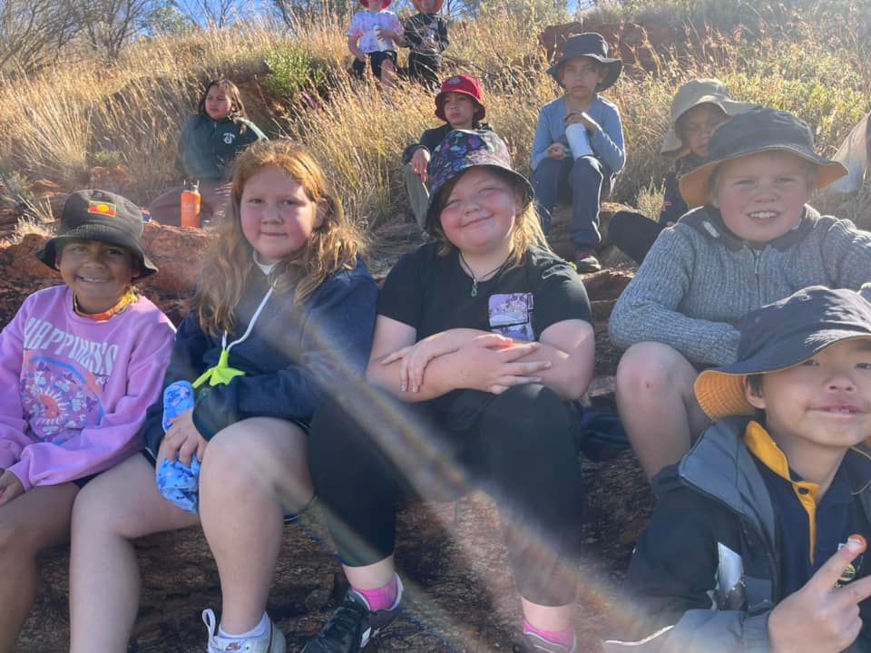 Group of children wearing hats sitting on a hill with dry grass.