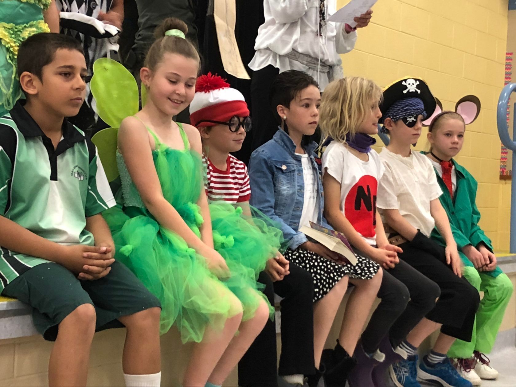 Children in costumes seated in a line; fairy, pirate, and Where's Waldo are visible.