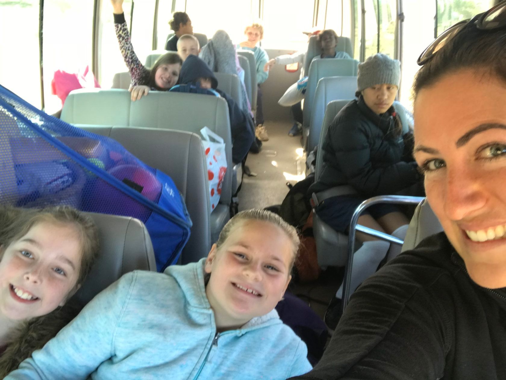 People on a bus. A woman and two girls smile in the front, others look at the camera from the seats.