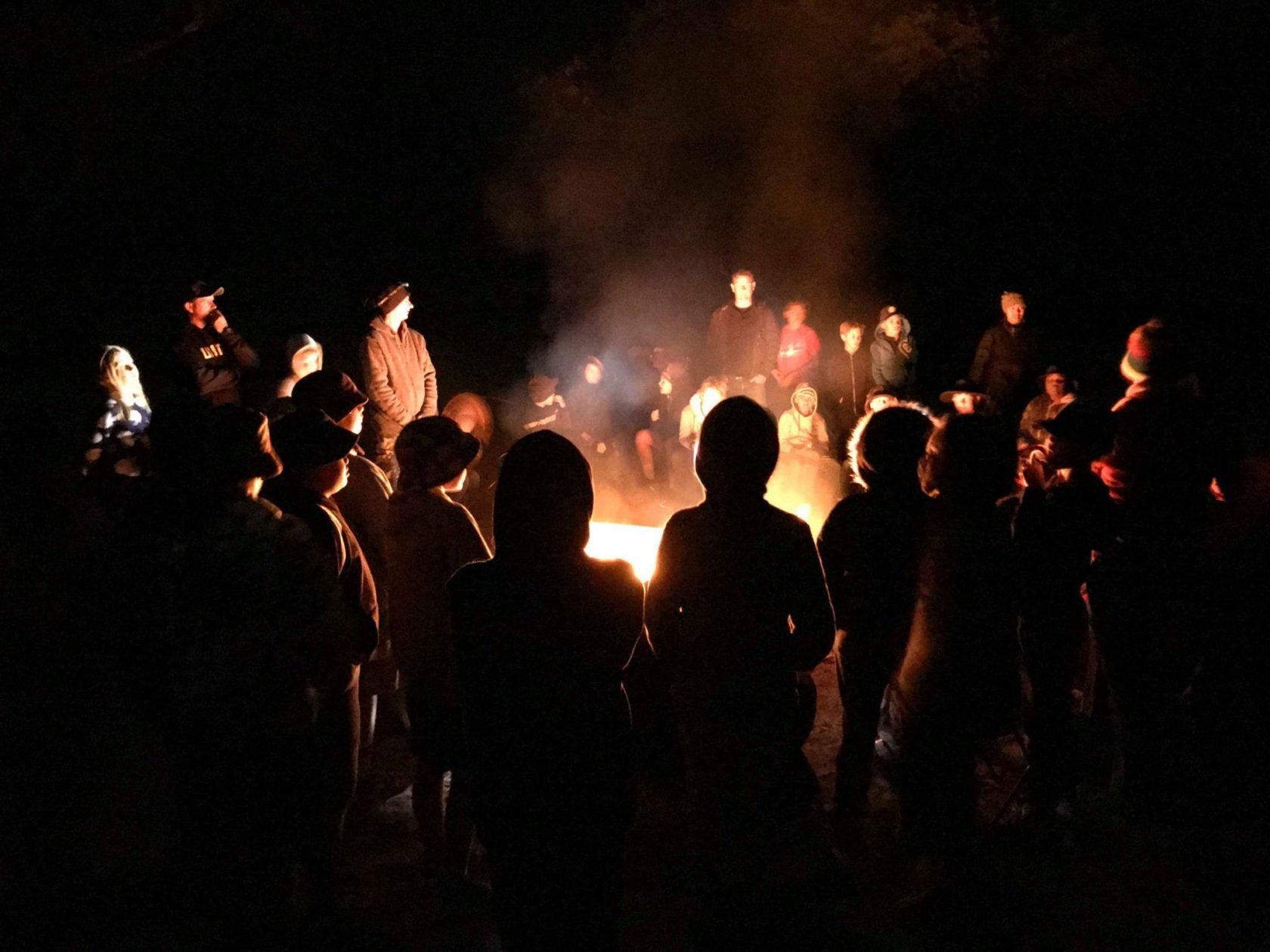 People gathered around a campfire at night; silhouetted figures with flames.