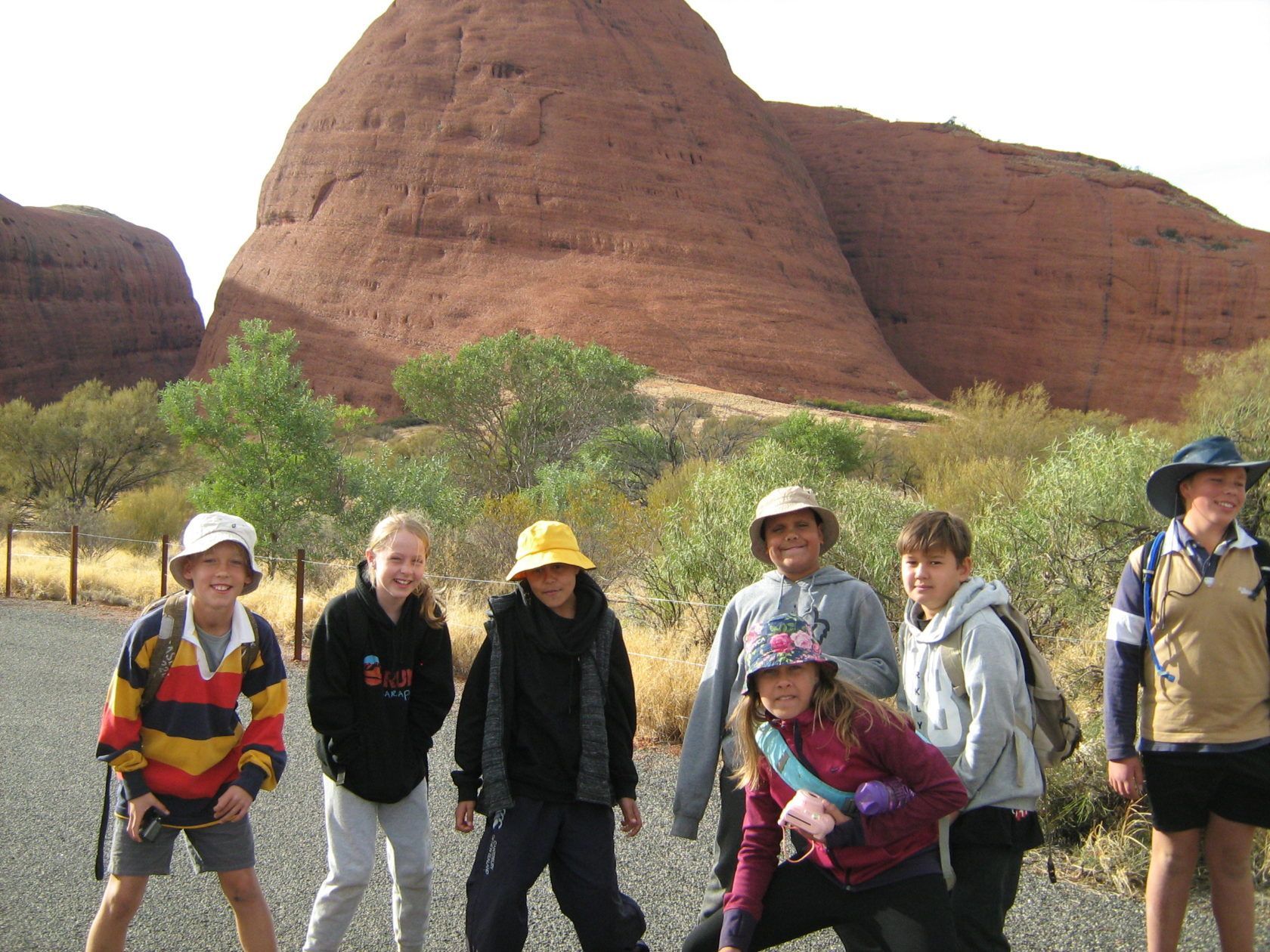 Children pose in front of a large, red rock formation. They wear hats and jackets.