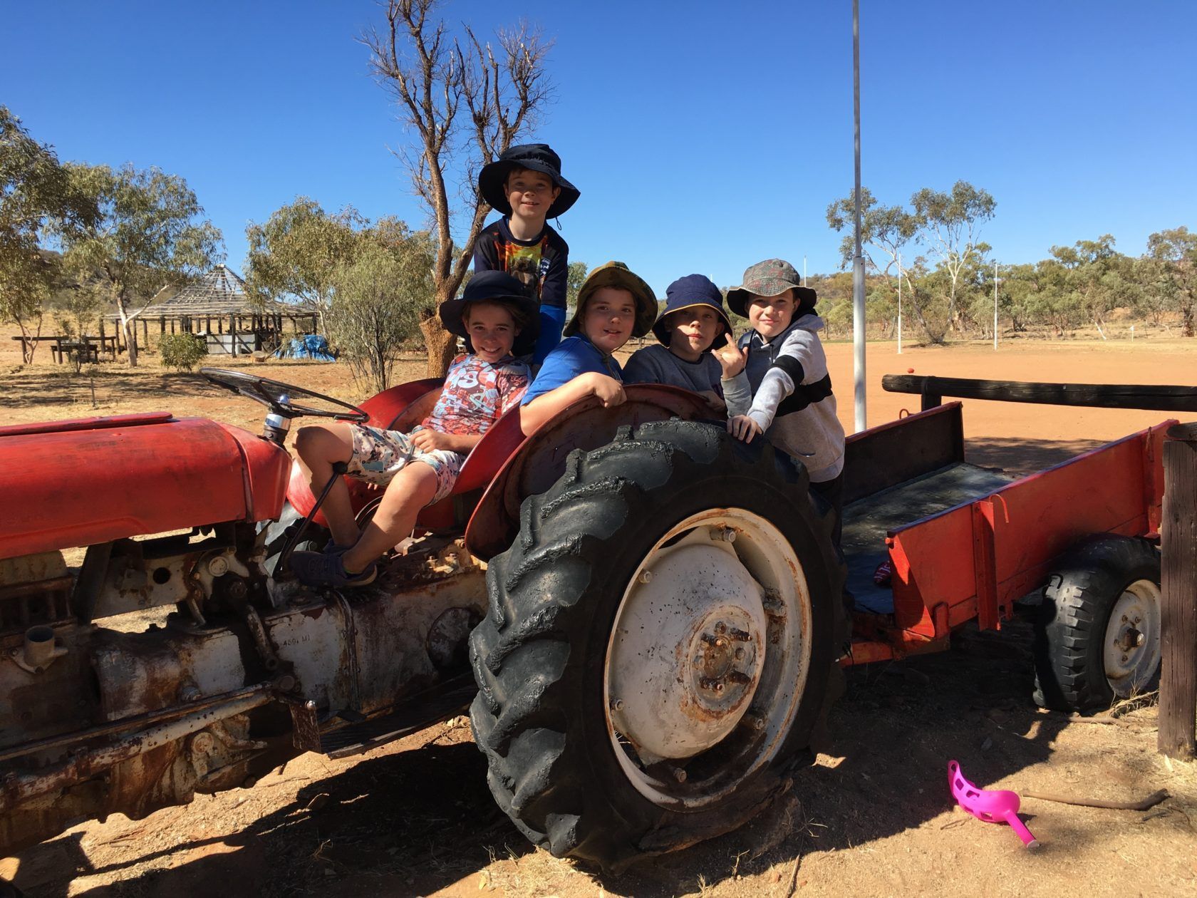 Children on a rusty red tractor in a sunny outdoor setting, smiling and playing.