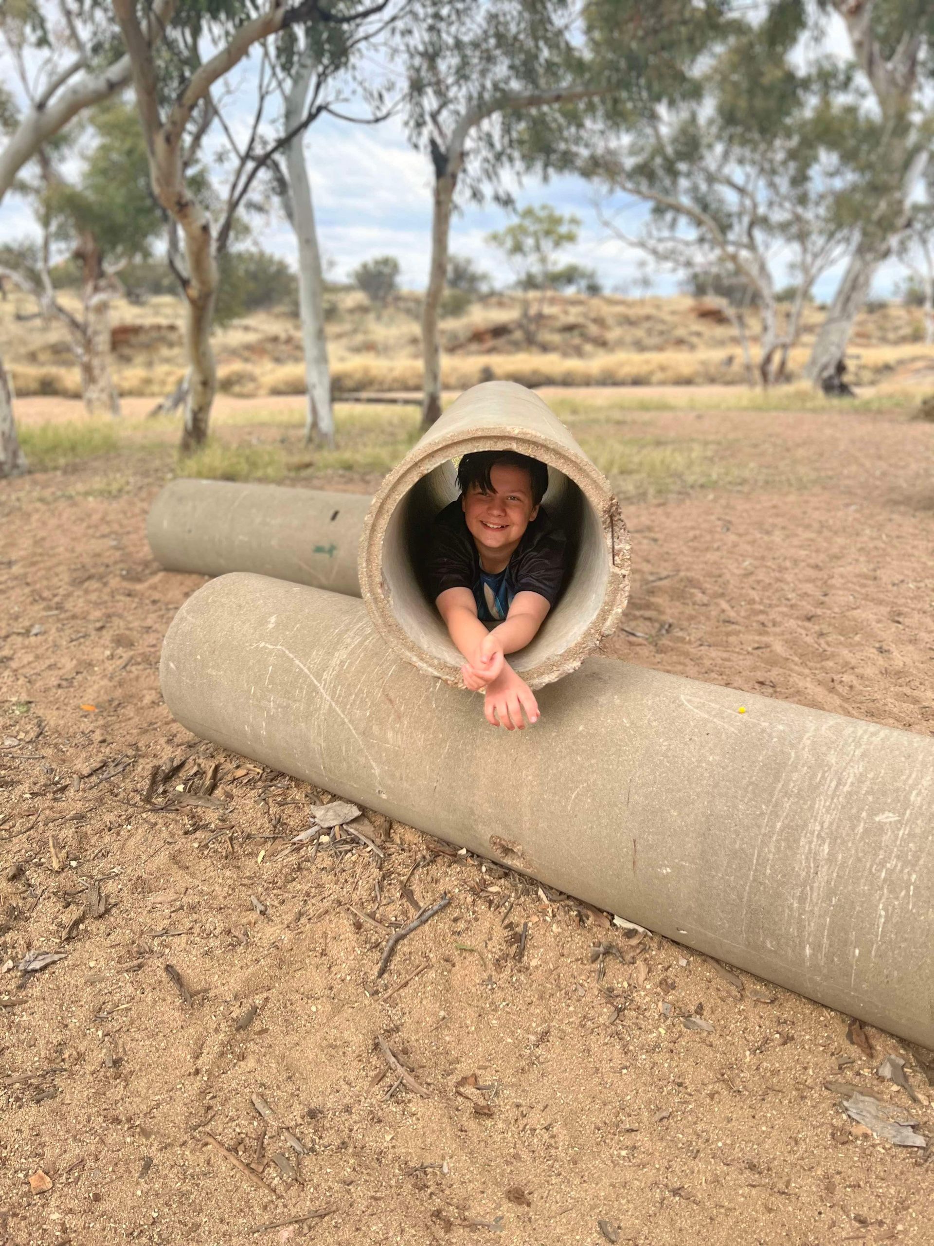 Child smiling, looking out from inside a concrete tube at a park.