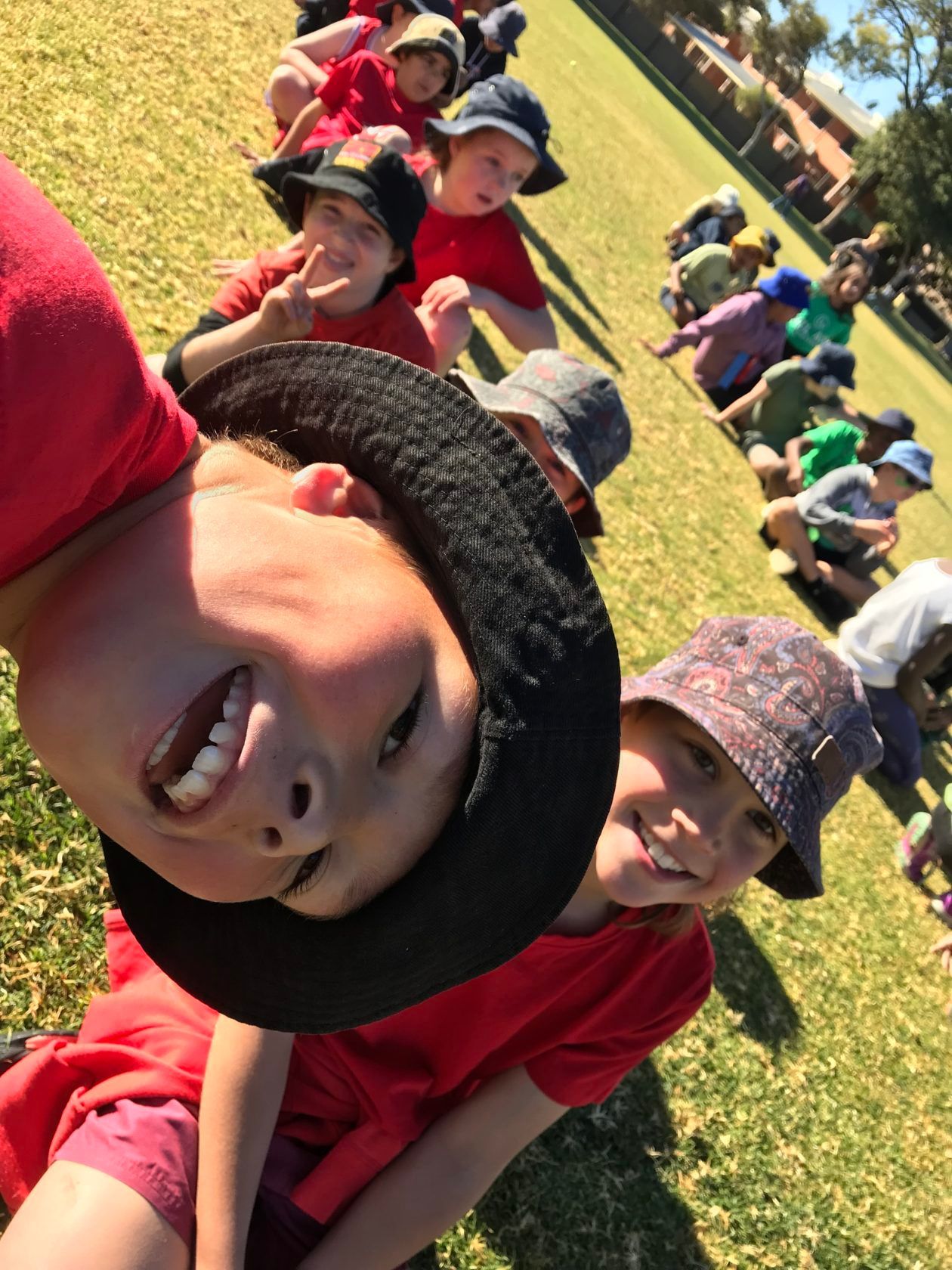 Children in red shirts and hats smiling on grass field.