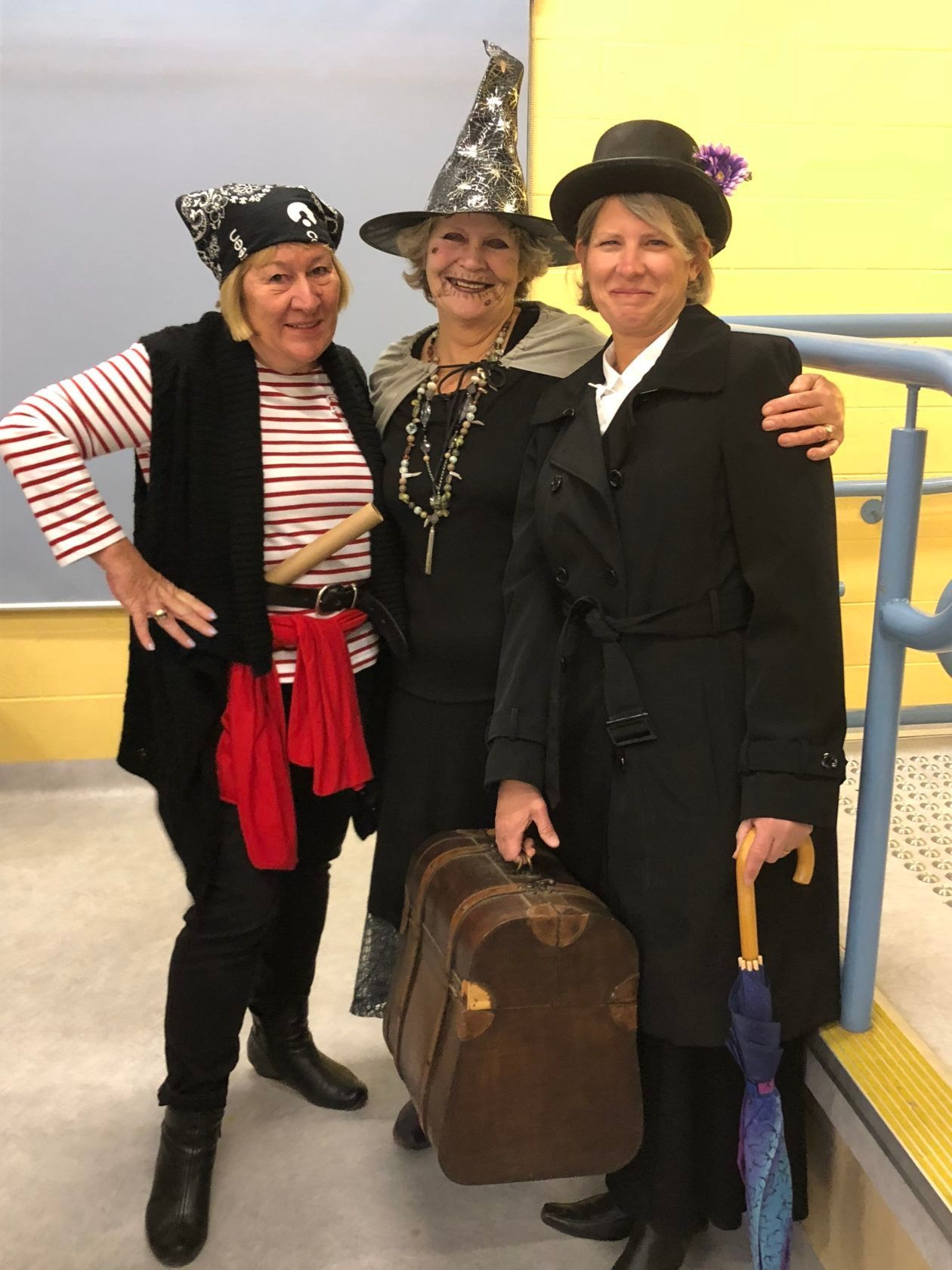 Three women in Halloween costumes: pirate, witch, and lady with suitcase.