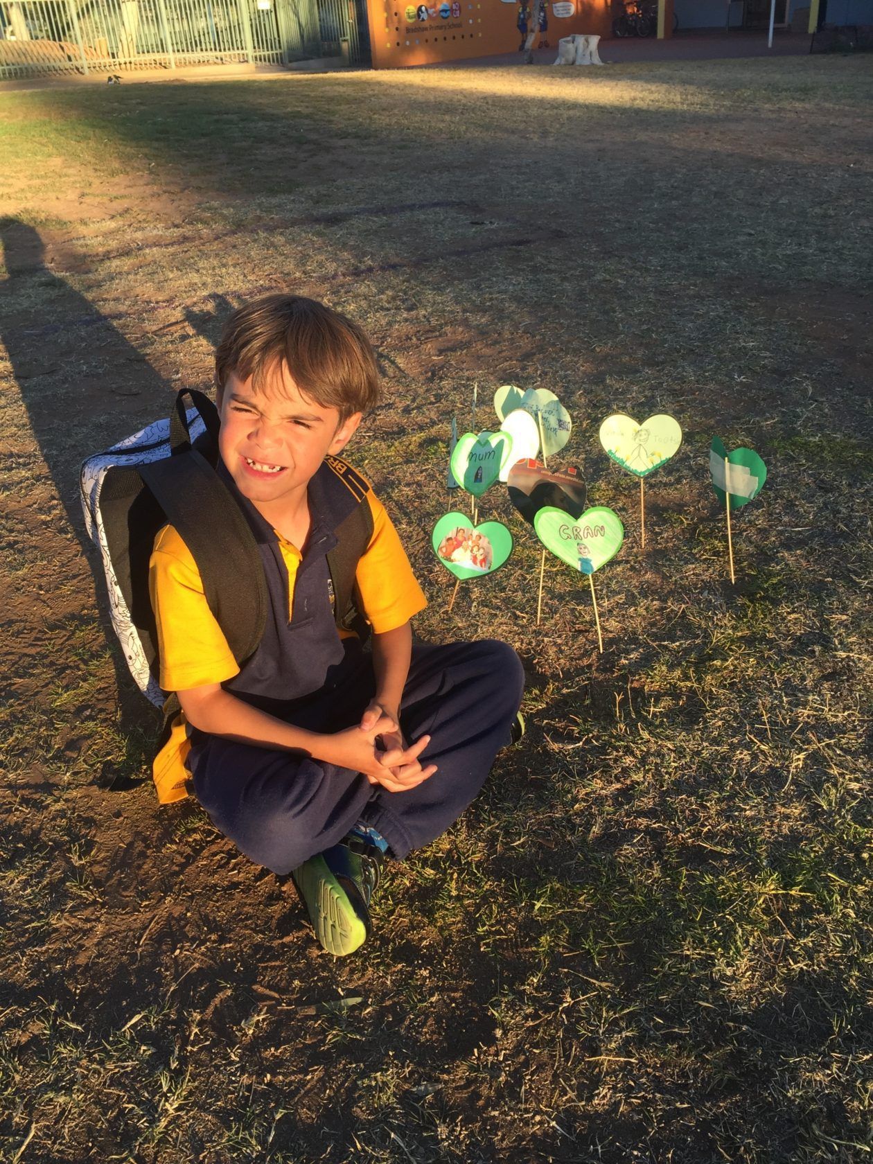 Boy in school uniform sits on grass with handmade heart decorations.