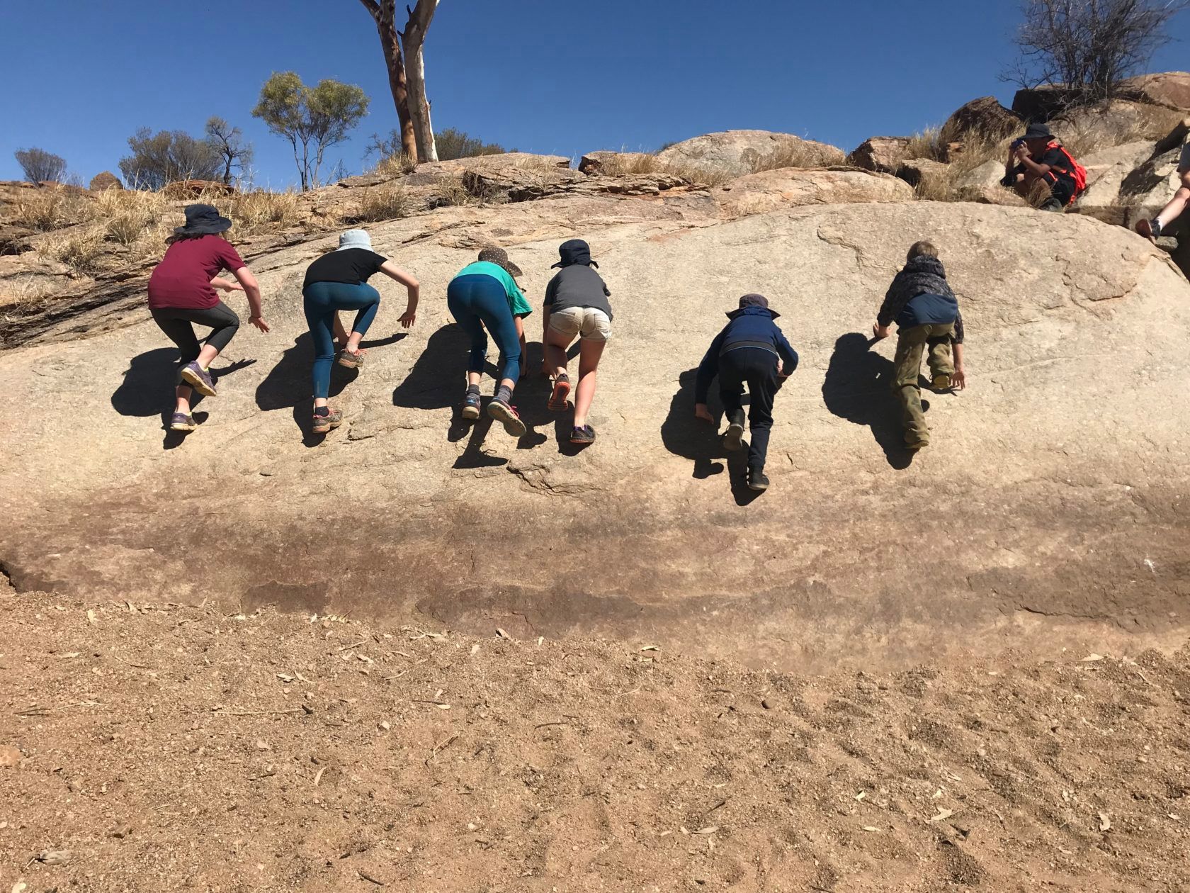 Children climbing a rock face in an outdoor setting on a sunny day.