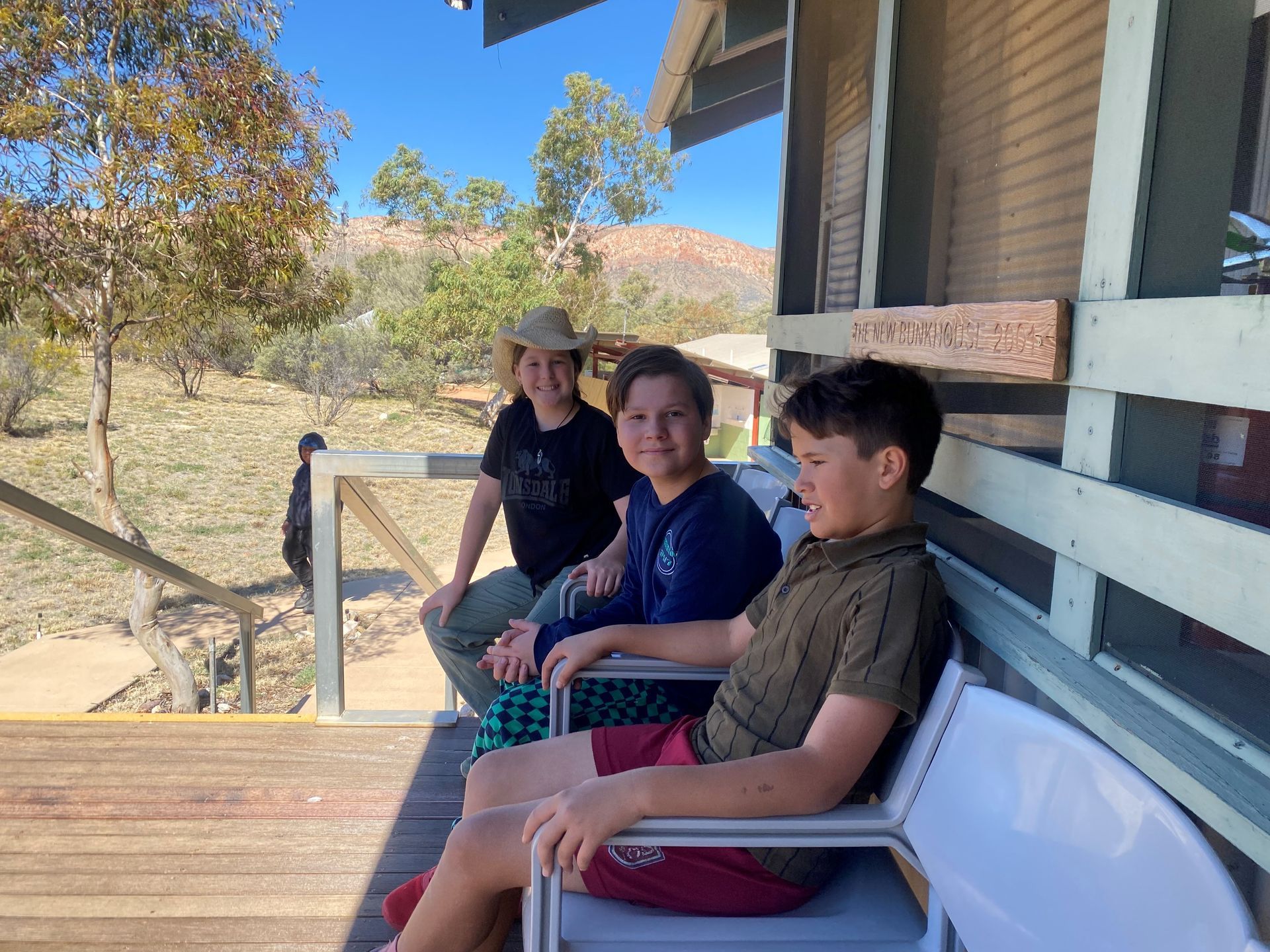 Three people sitting on a porch in a sunny outdoor setting, smiling.