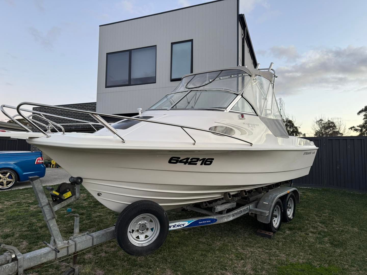 White boat on a trailer in front of a modern house.