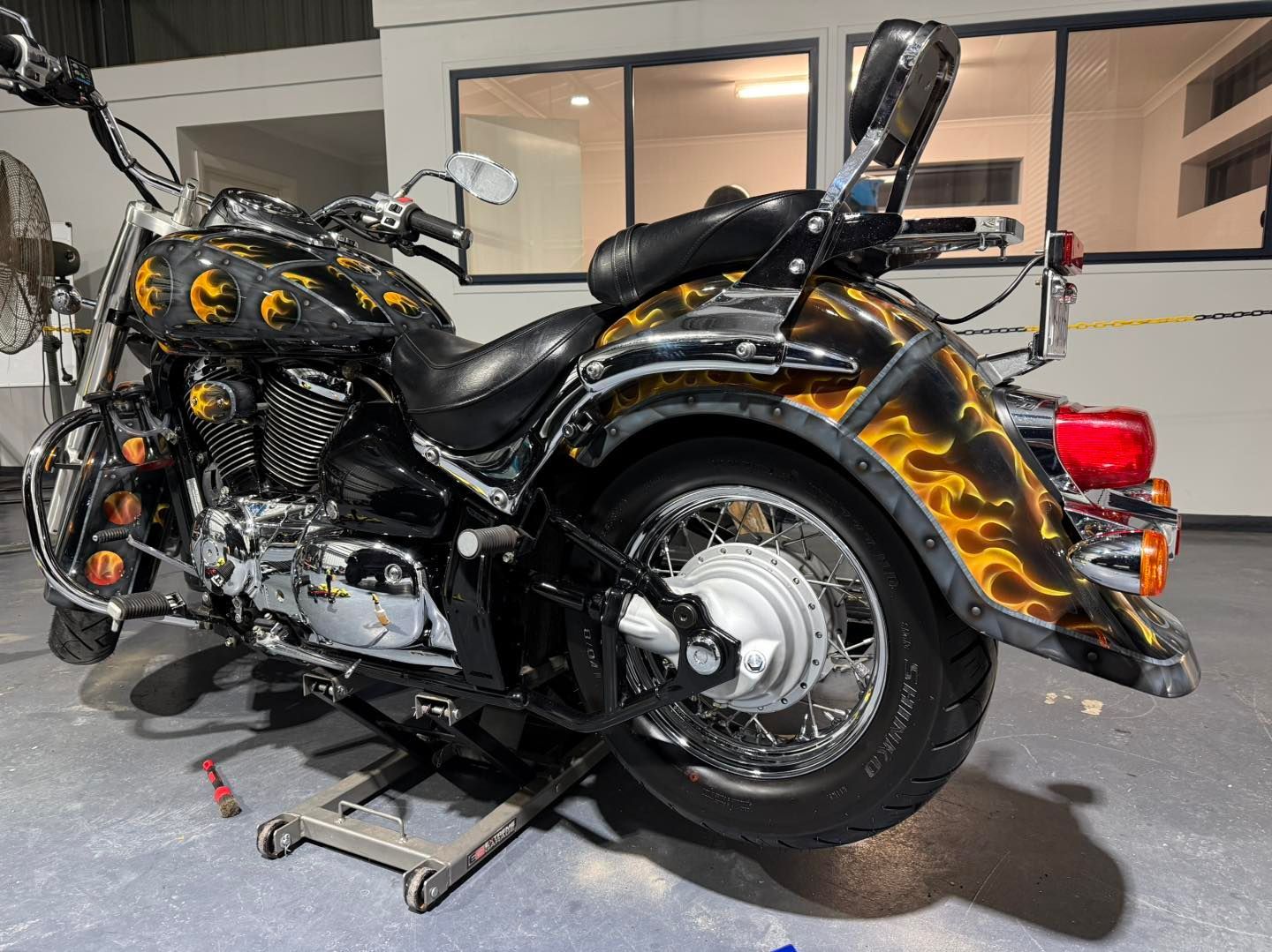 Black and chrome motorcycle with flame-themed paint, propped on a lift, in a garage.