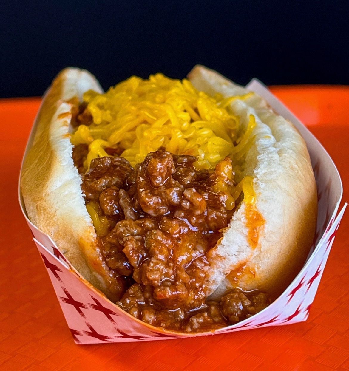 A chili cheese hot dog on a bun sitting on a piece of aluminum foil against a dark background.