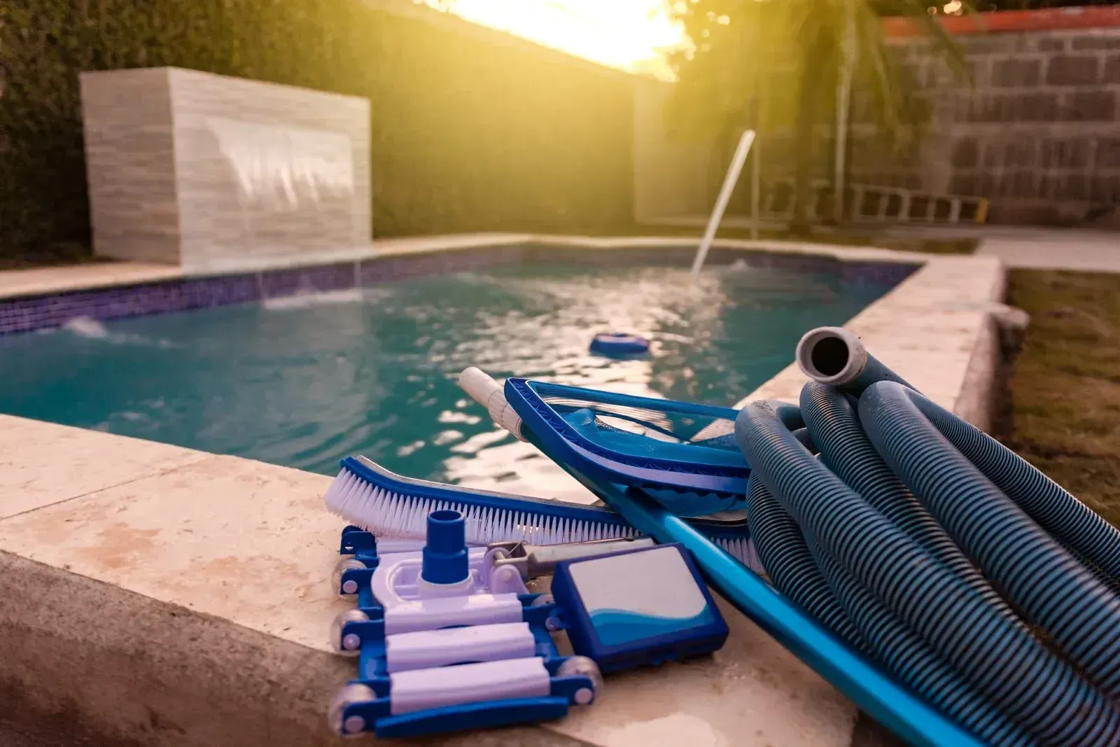 Pool with cleaning tools laid out on the edge: brush, vacuum head, and hose.