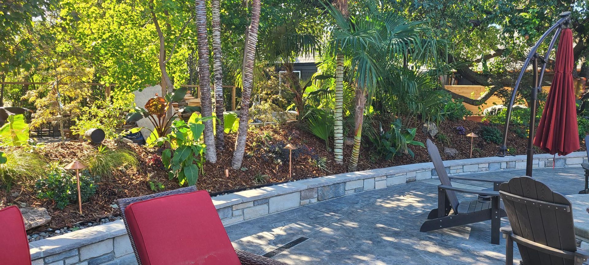 Patio with red lounge chair, trees, and an umbrella.