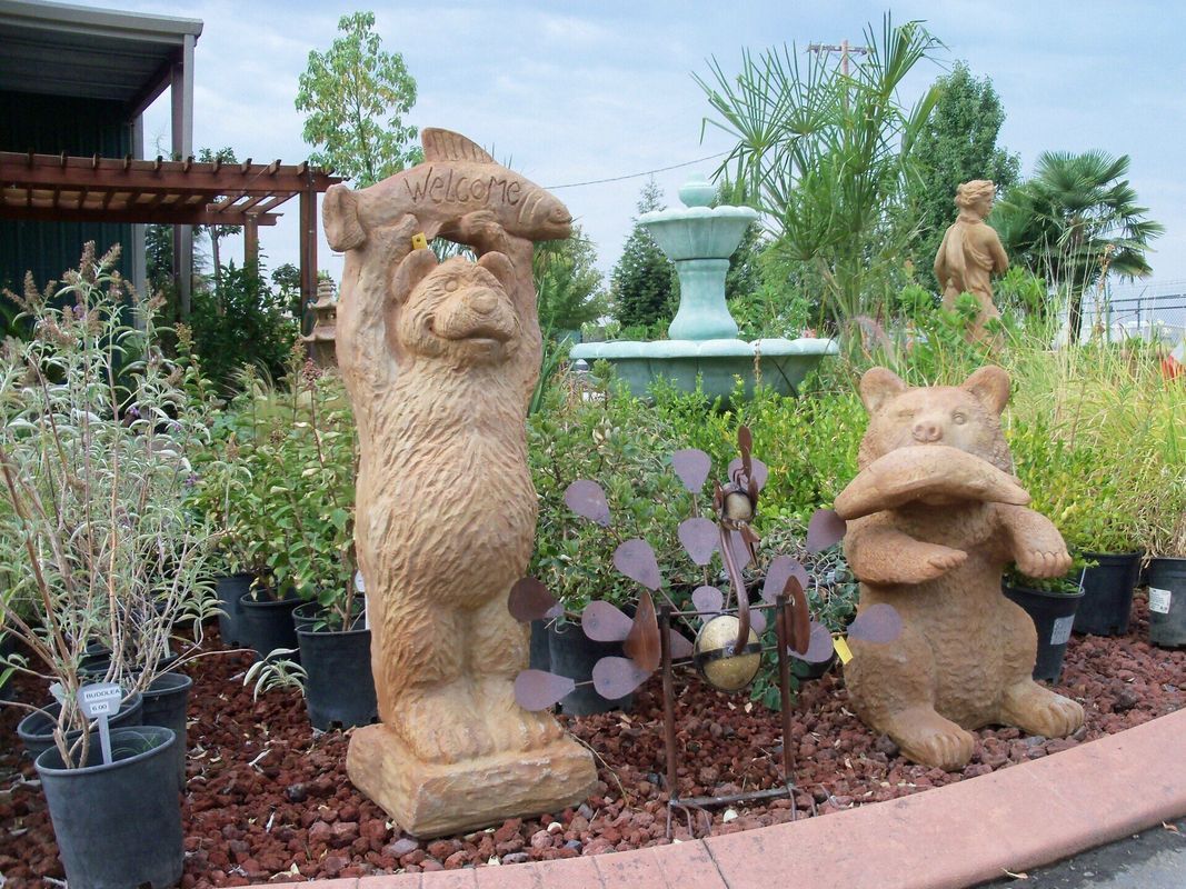 Statues of bears holding fish near a fountain in a garden.