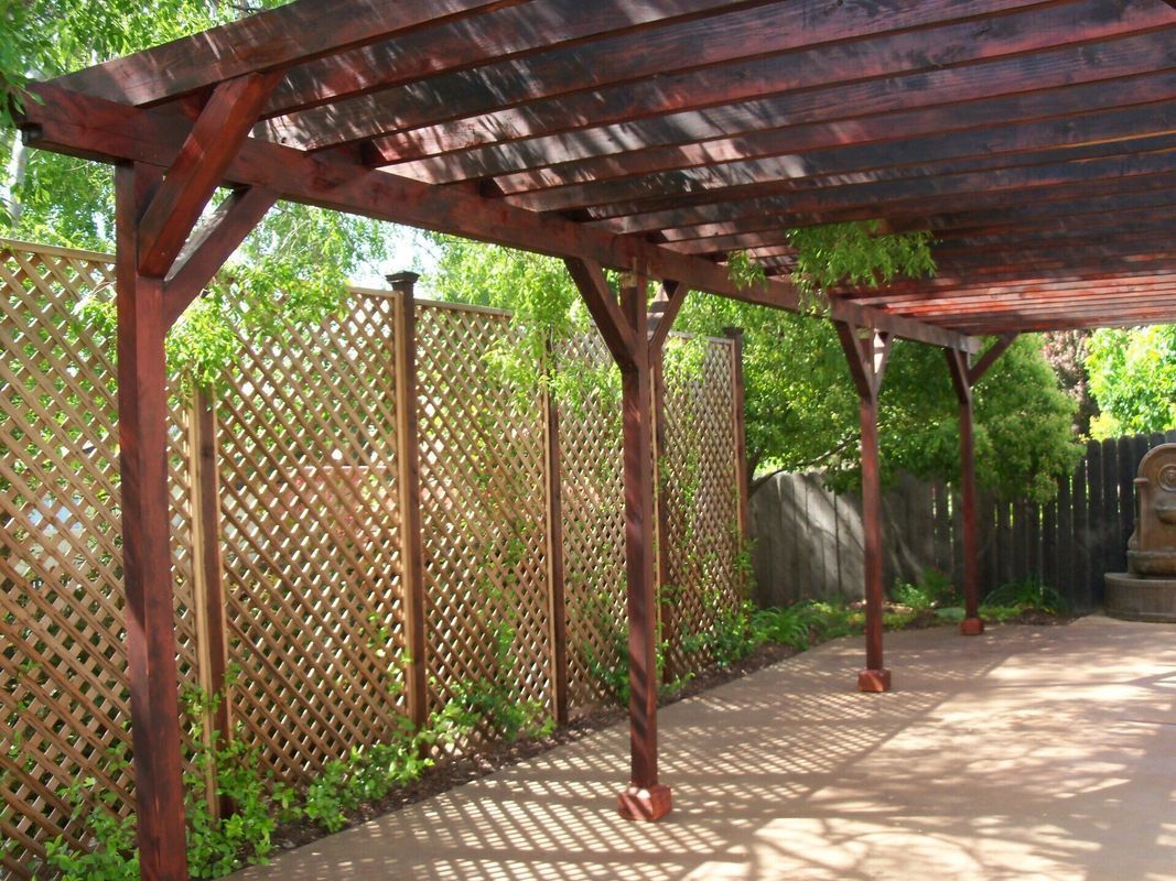 Brown pergola with lattice fence and concrete patio.