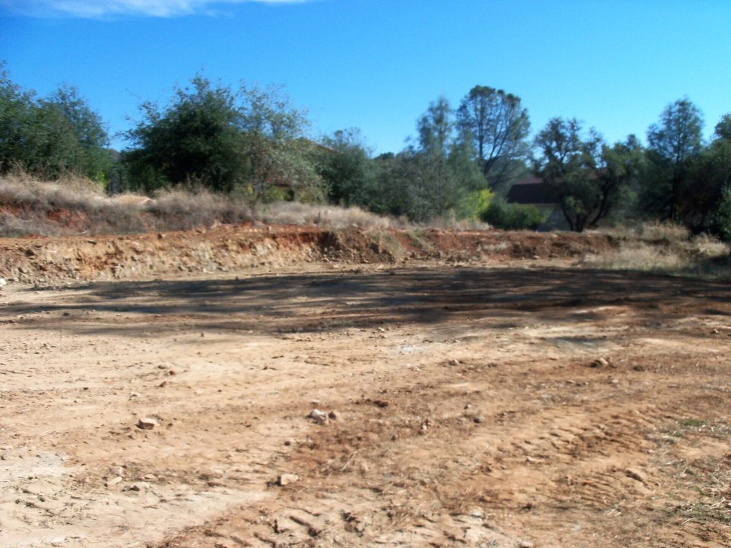 Brown dirt clearing with a small ridge of earth and trees in the background under a blue sky.