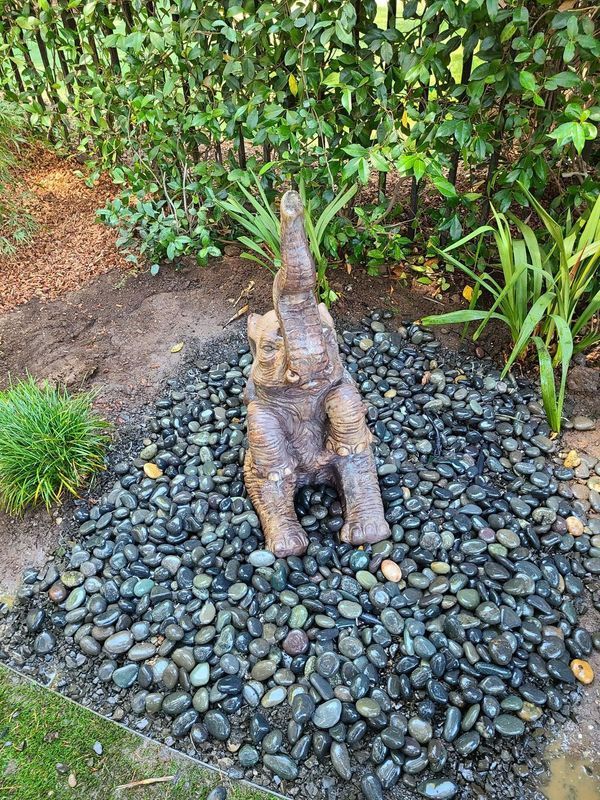 Bronze elephant statue on a bed of dark grey stones in a garden.