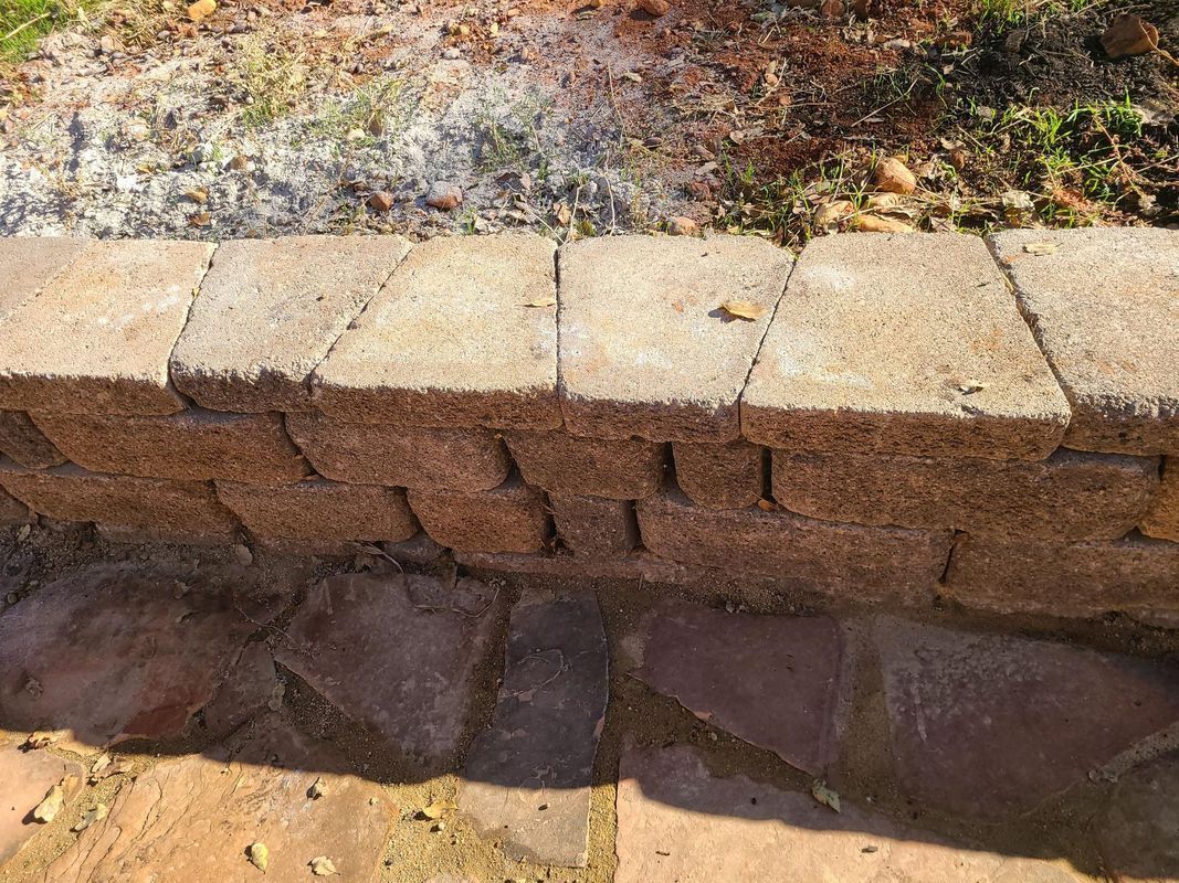 Stone retaining wall with a weathered appearance, constructed from interlocking blocks.