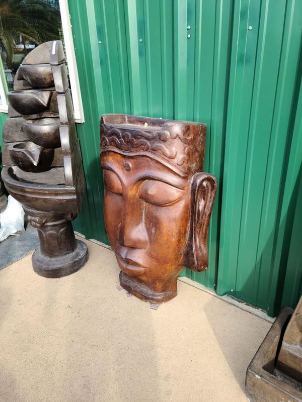 Wooden Buddha head sculpture on the floor, next to a green wall.