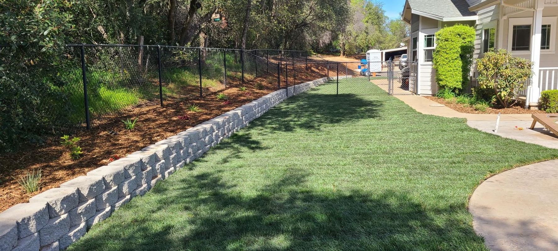A lawn with a retaining wall and fence near a house.