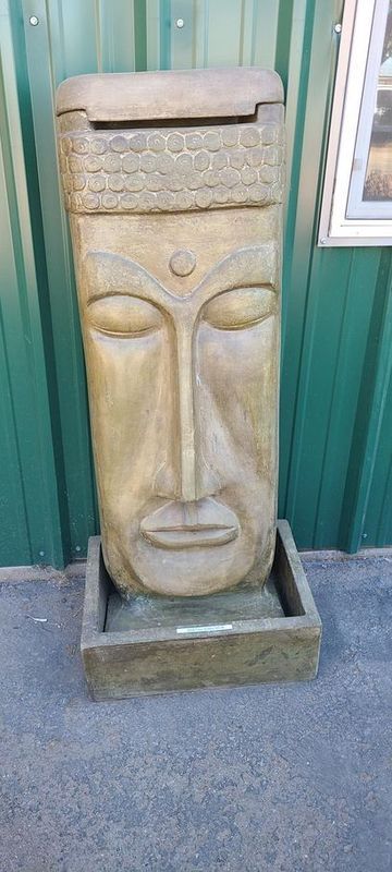 Statue of a face with closed eyes, in a vertical column with a box at the bottom.