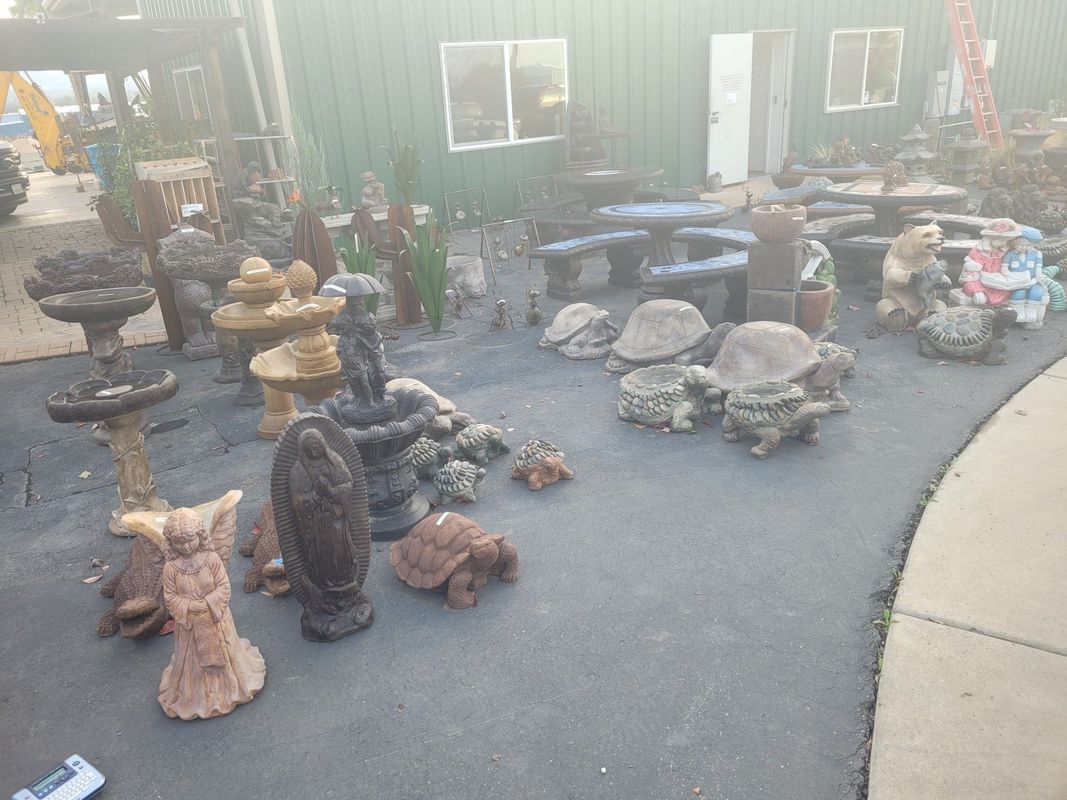 Outdoor display of garden statues, fountains, and seating in front of a green building.