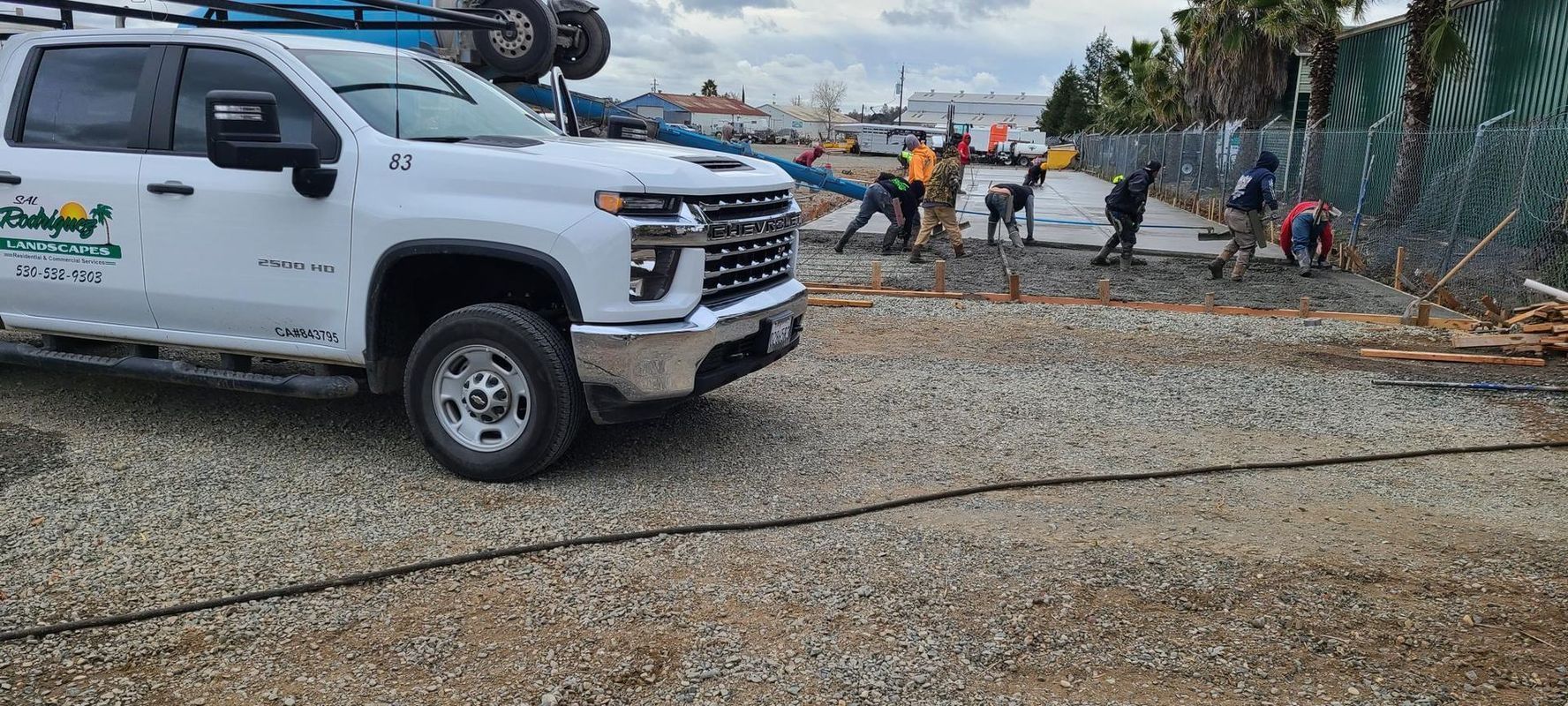 White truck with workers building a fence in a gravel area.