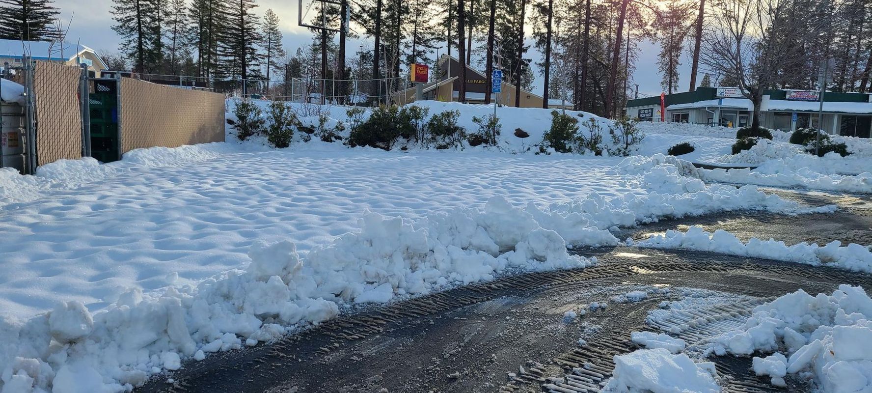 Snowy scene with road and houses. Trees and structures in the background, daytime.