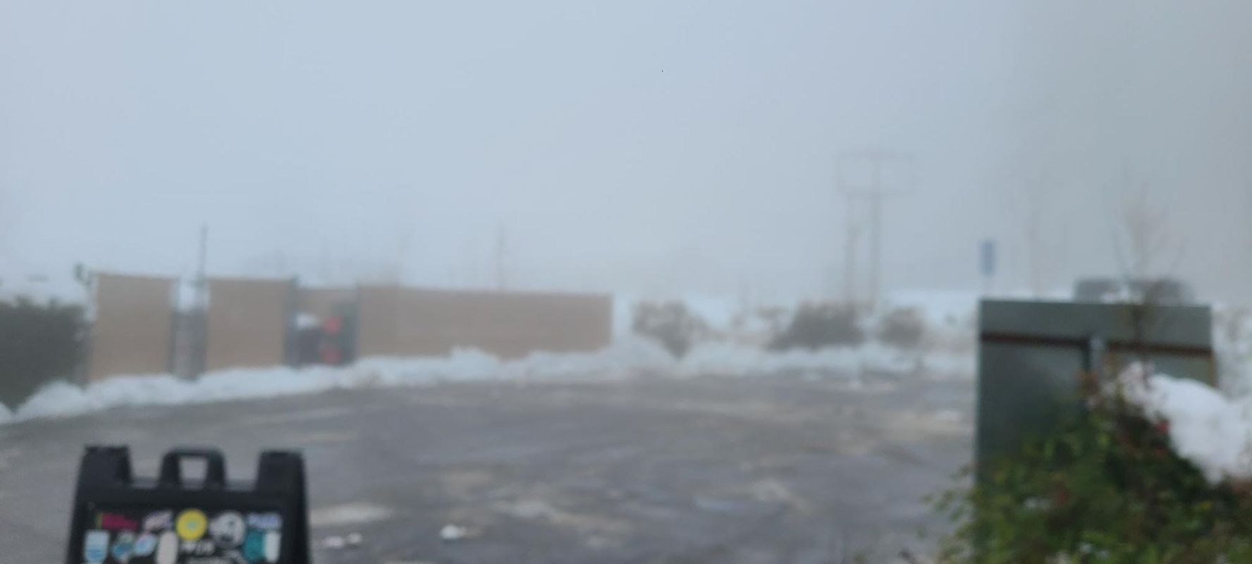 A snowy day with a sign, building, and utility poles obscured by fog.