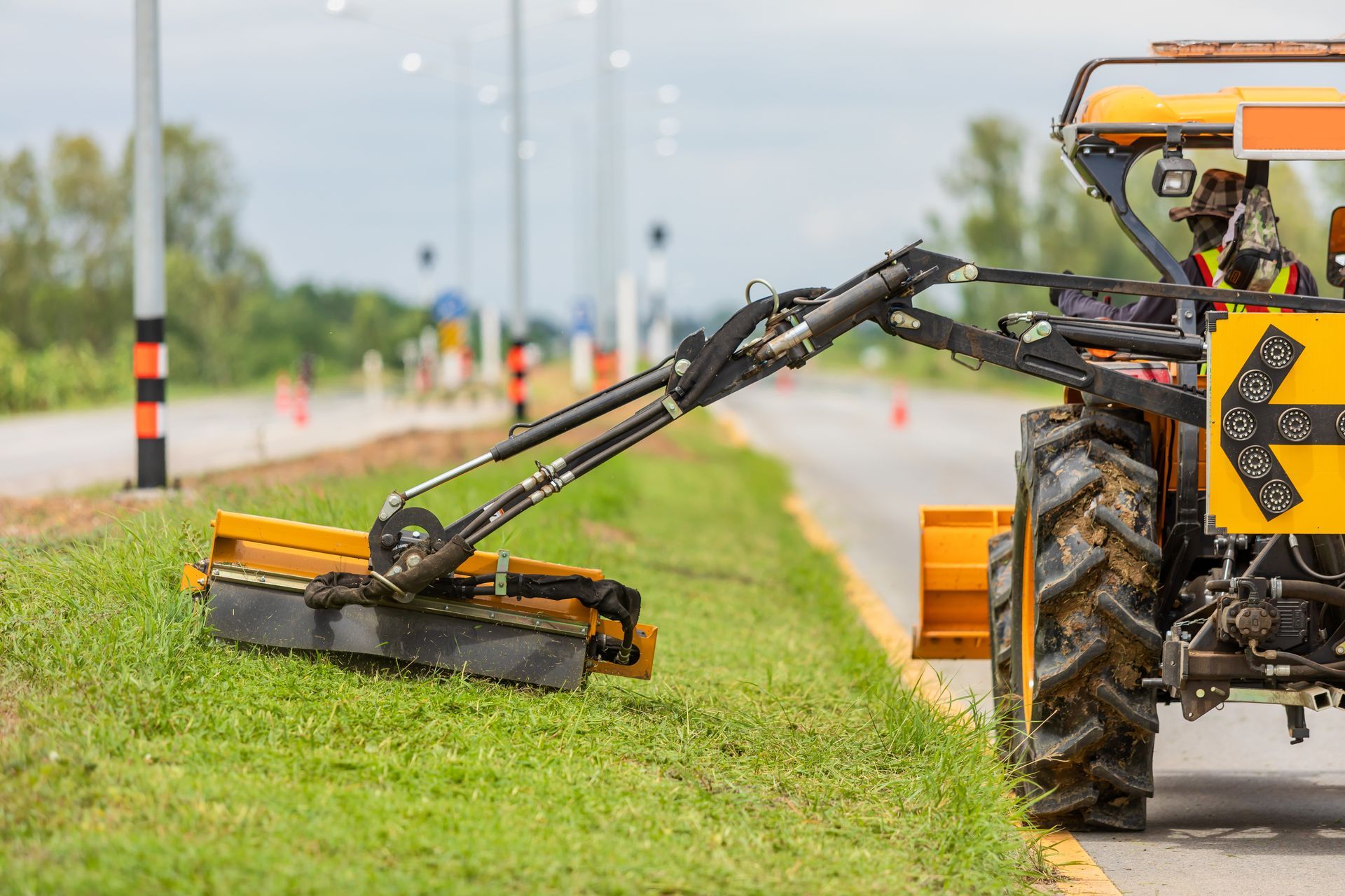 Yellow tractor mowing roadside grass.