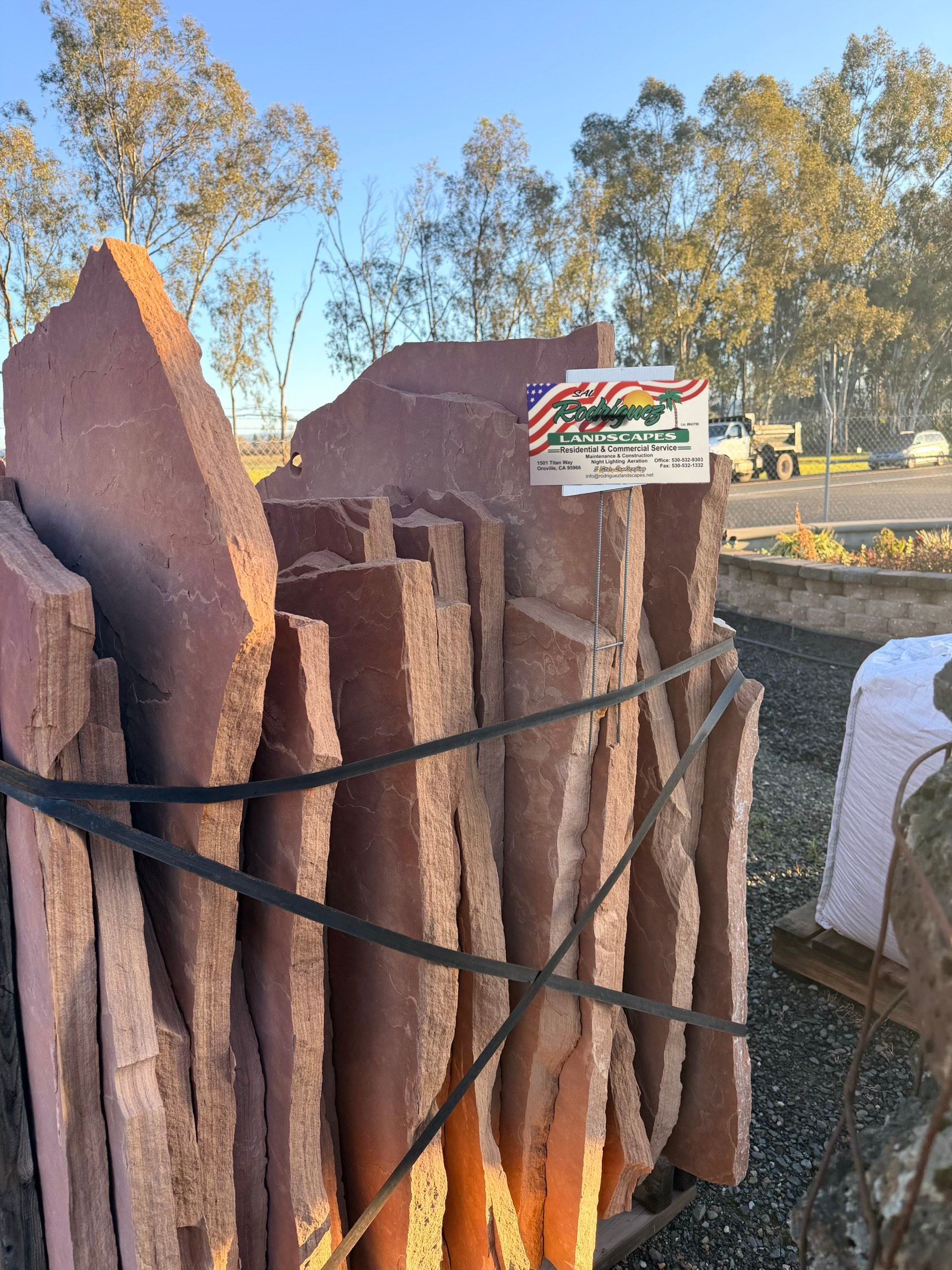 A bundle of reddish-brown flagstone slabs secured with black straps, outdoors in a yard.