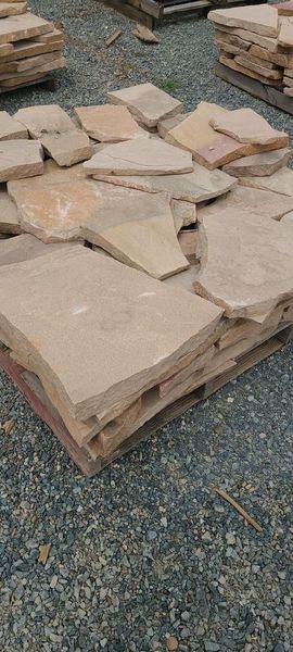 Pile of irregular tan stone pavers on a wooden pallet, resting on a bed of gravel.
