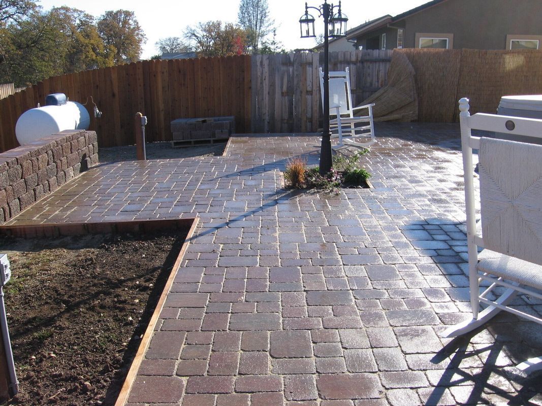 Brick patio with wooden fence, lamp post, and white chairs.
