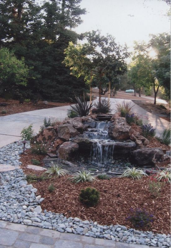 Water feature with a small waterfall surrounded by rocks and plants, on a path.