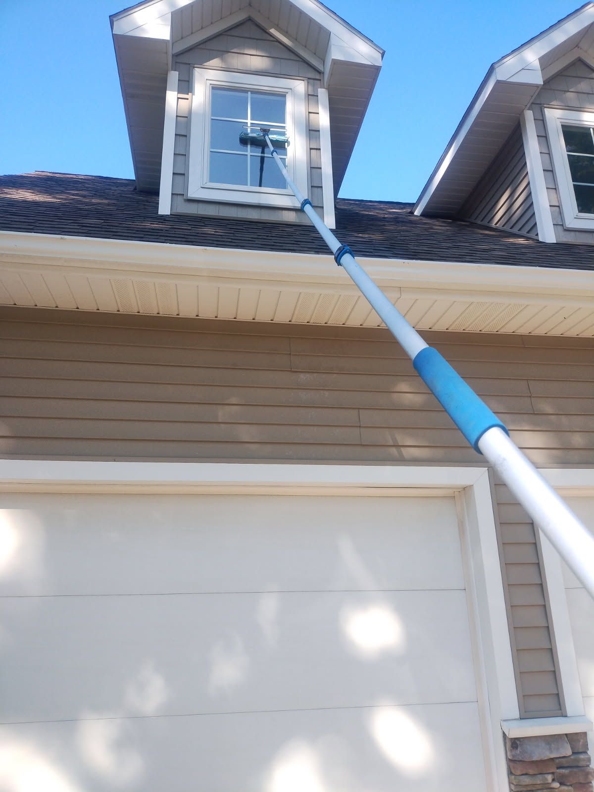 Window being cleaned on a house with a long pole.