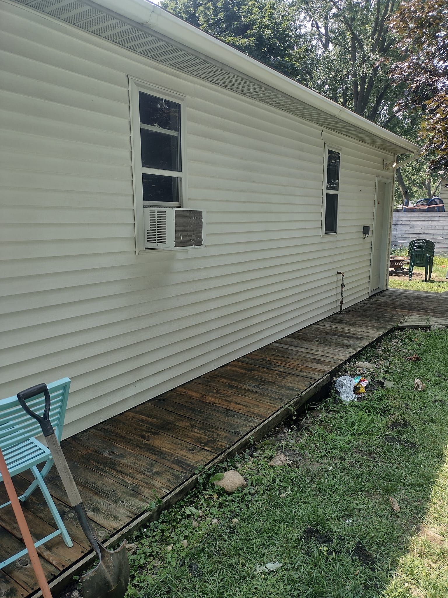 Side of a white-sided building with two windows, a small deck, and a grassy area.