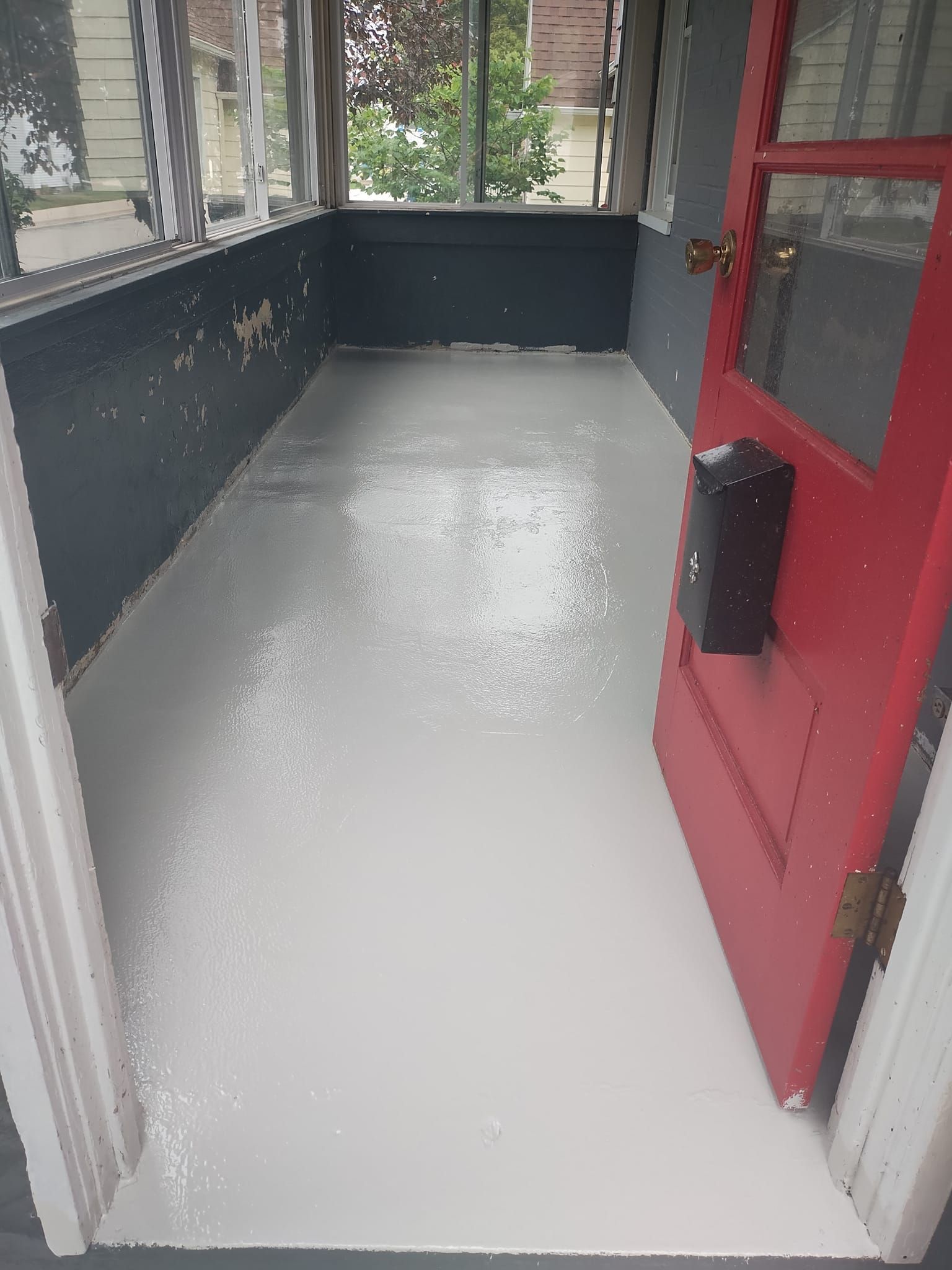A sunroom with a light gray floor, red door, and dark gray walls.