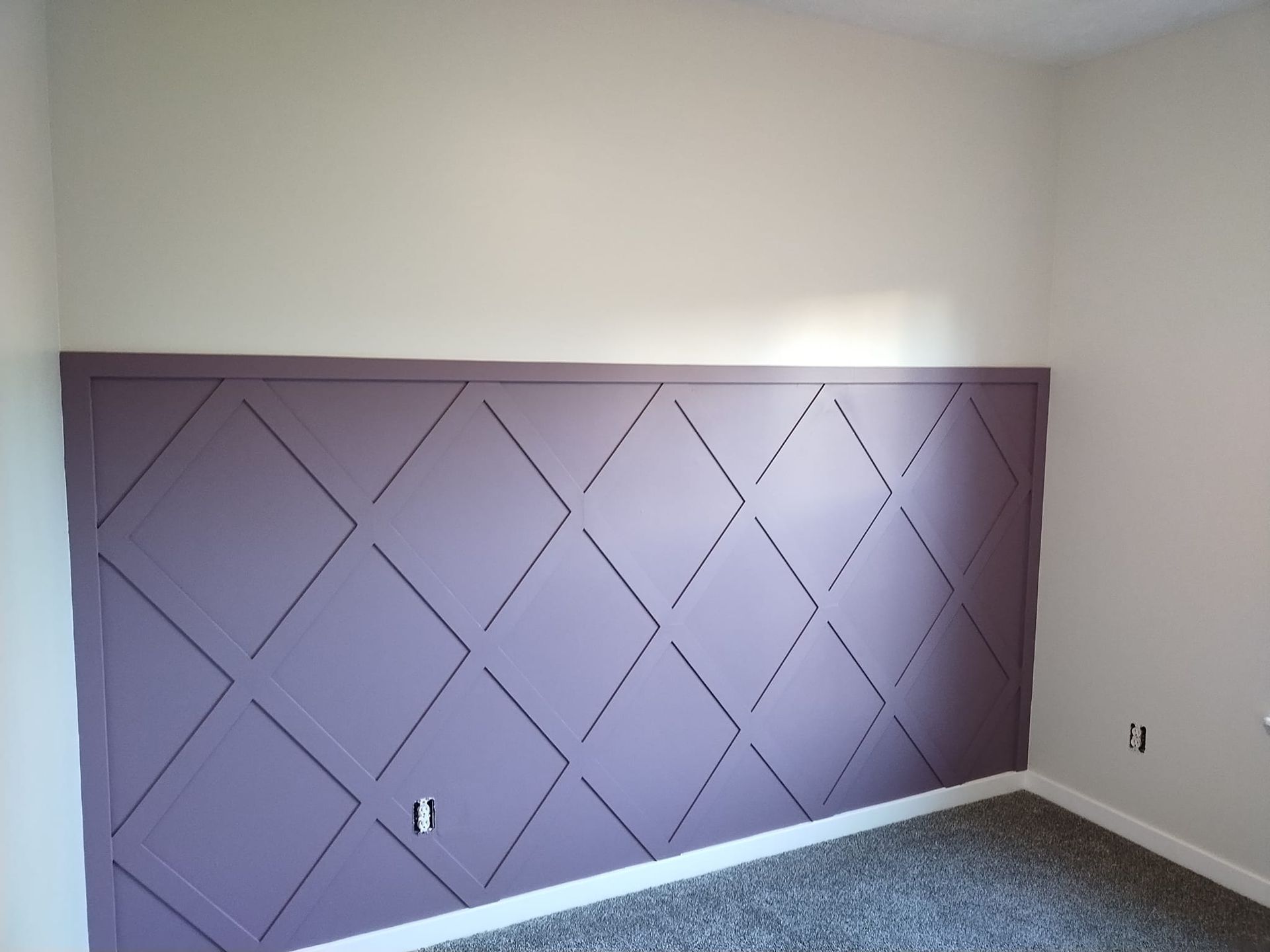 Purple diamond-patterned accent wall in a room with off-white walls and gray carpet.