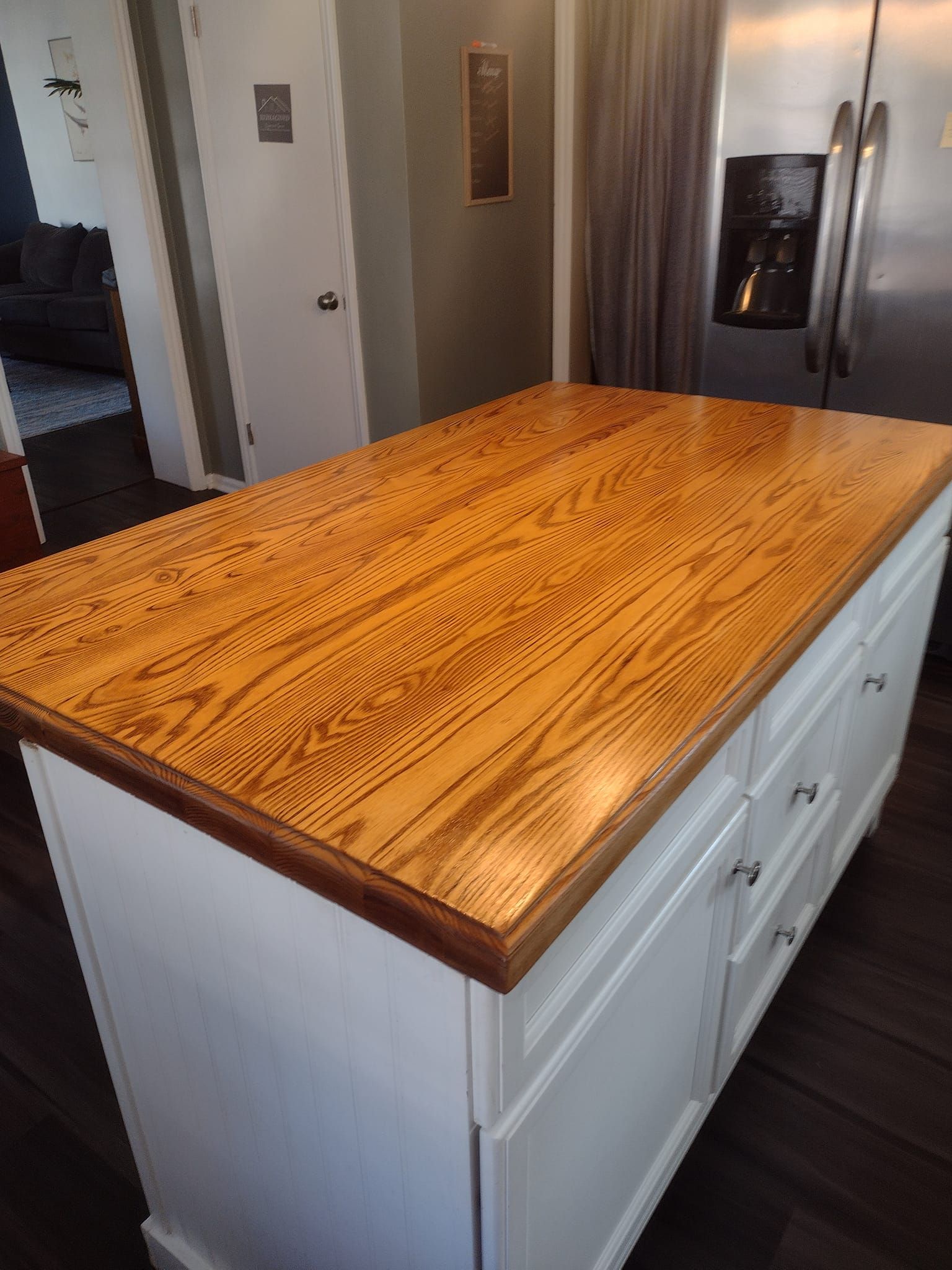 Kitchen island with a wood countertop, white cabinets, and stainless steel refrigerator.